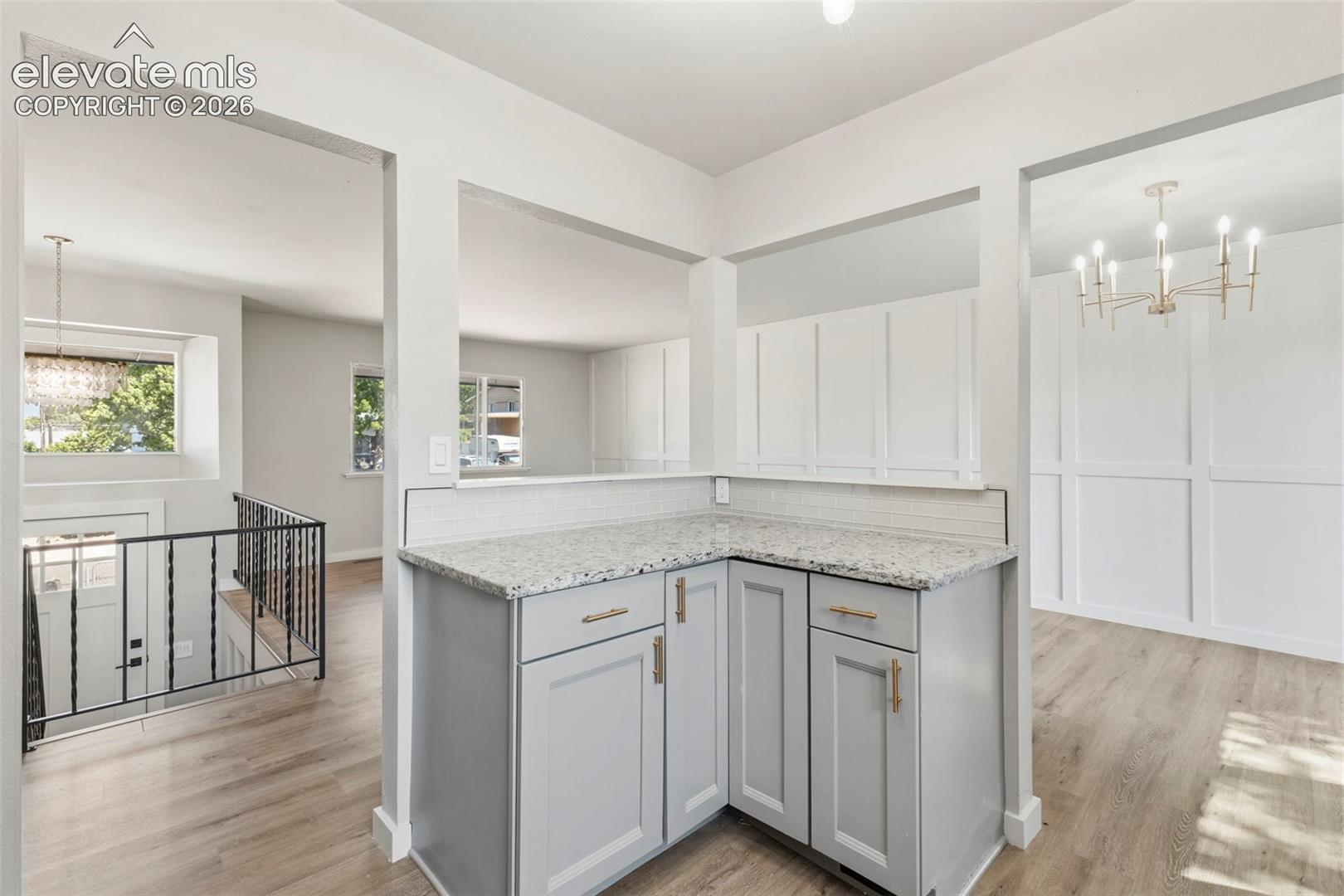 Corner peninsula featuring gray cabinetry with gold hardware, granite countertop, and glass subway tile backsplash passthrough for entertaining and maintaining natural light