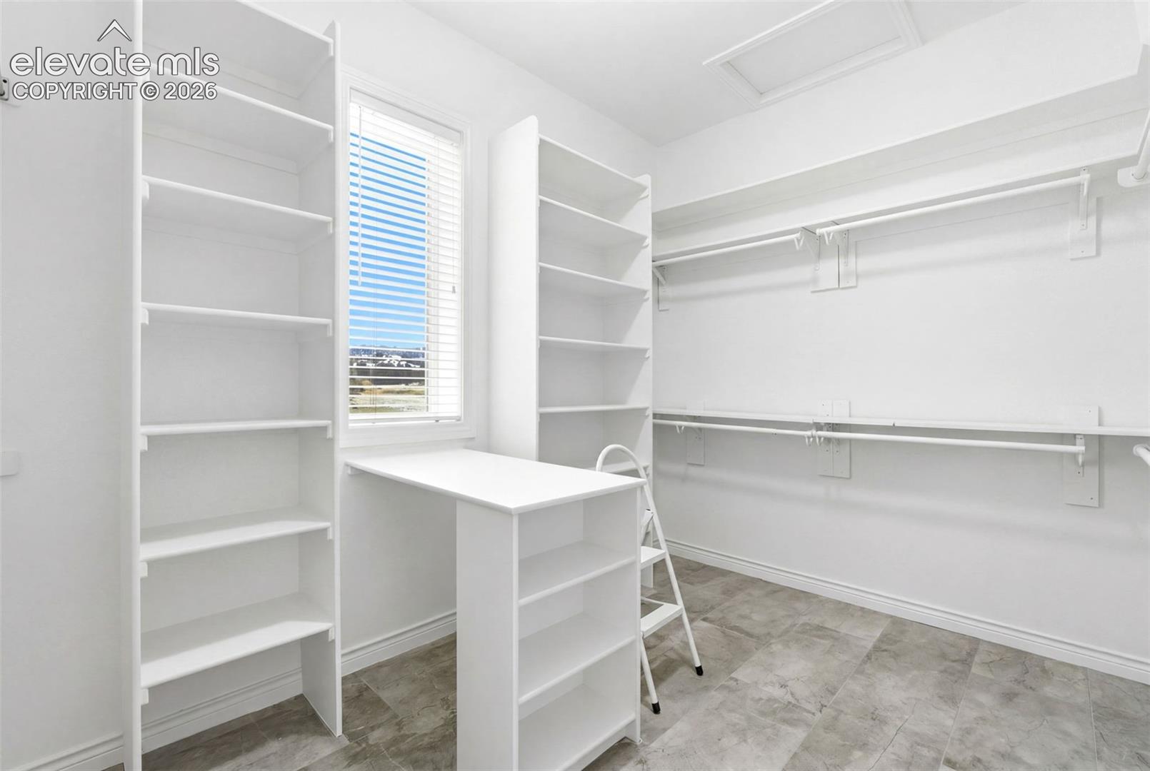 Built-in shelving units, integrated desk space, a window with blinds, clothing rods, and tile flooring