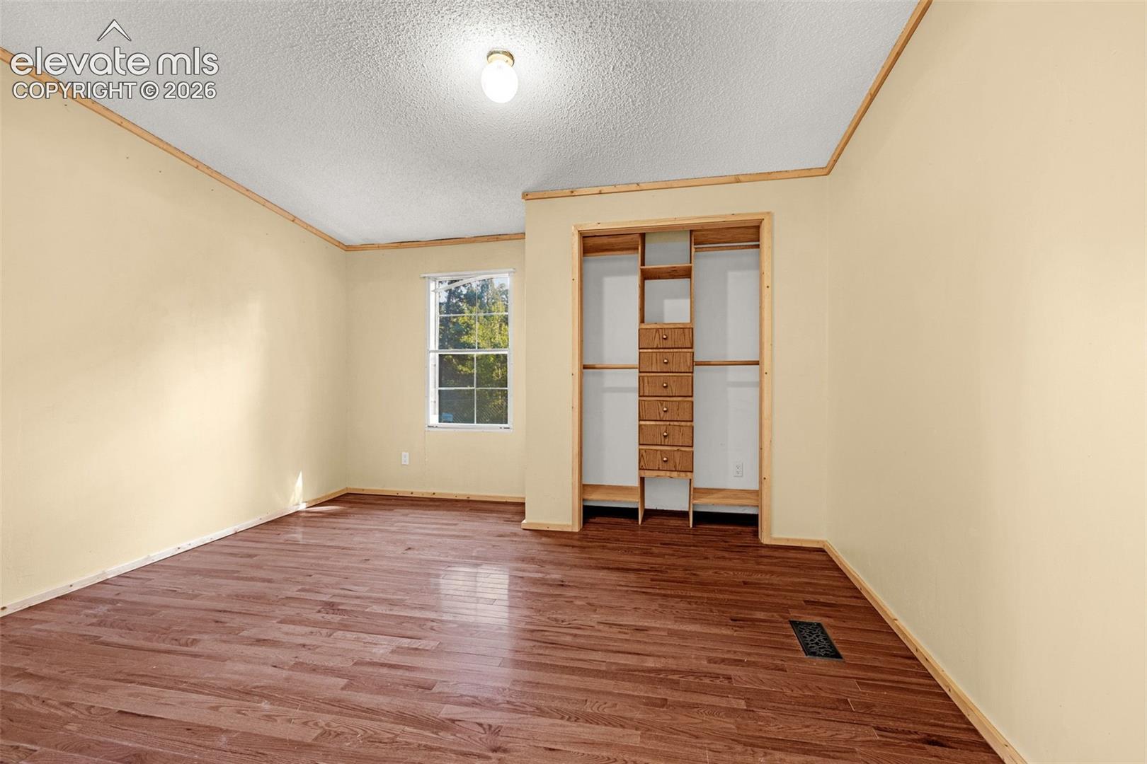 Wood-finish flooring, built-in closet organization, fixed window, and a flush mount ceiling light fixture