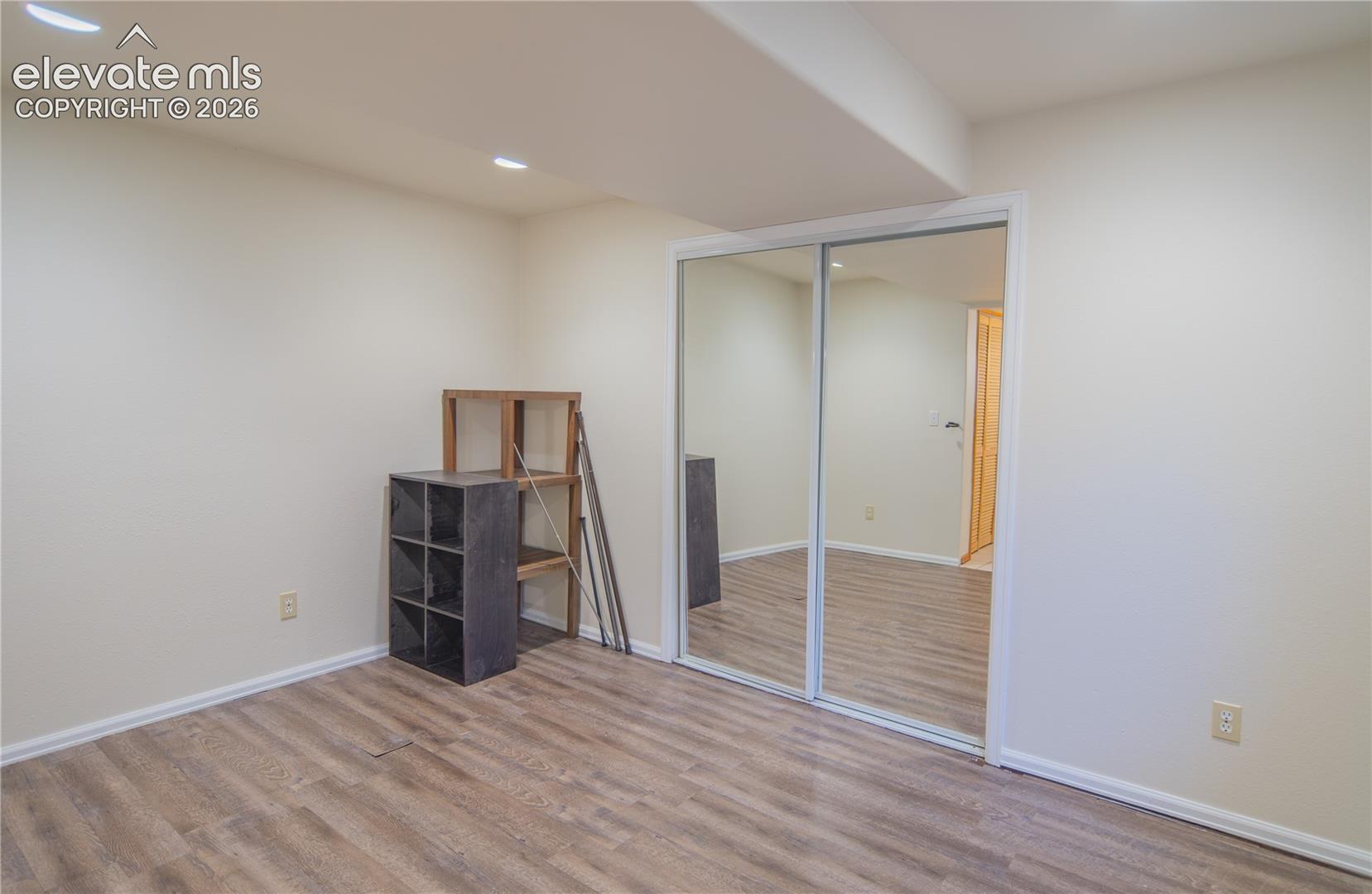 Versatile lower-level bedroom with wood-look flooring, recessed lighting, and a mirrored closet.