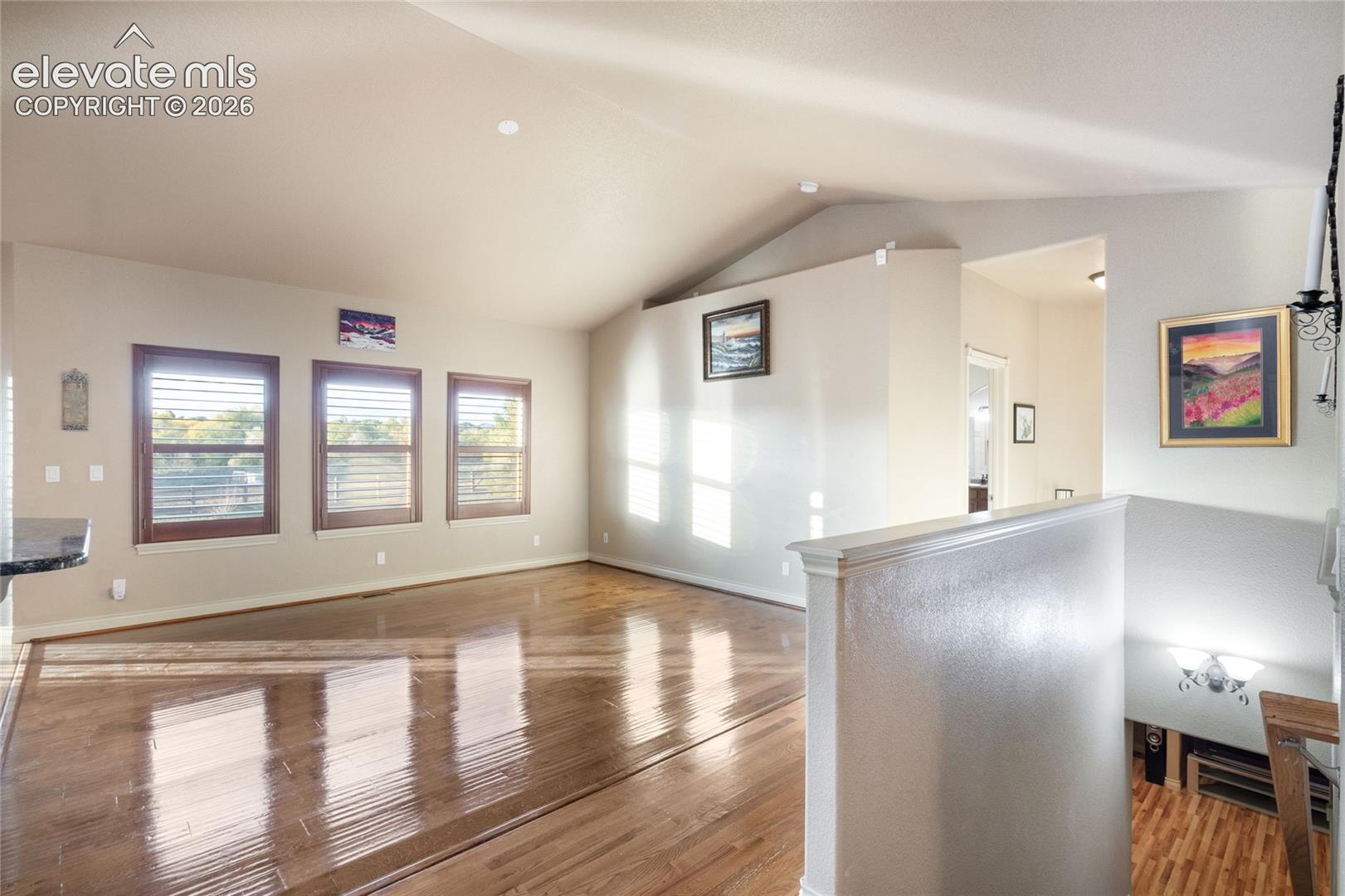 Vaulted ceilings, wood-finish flooring, three windows with plantation shutters, stairs to basement on the right