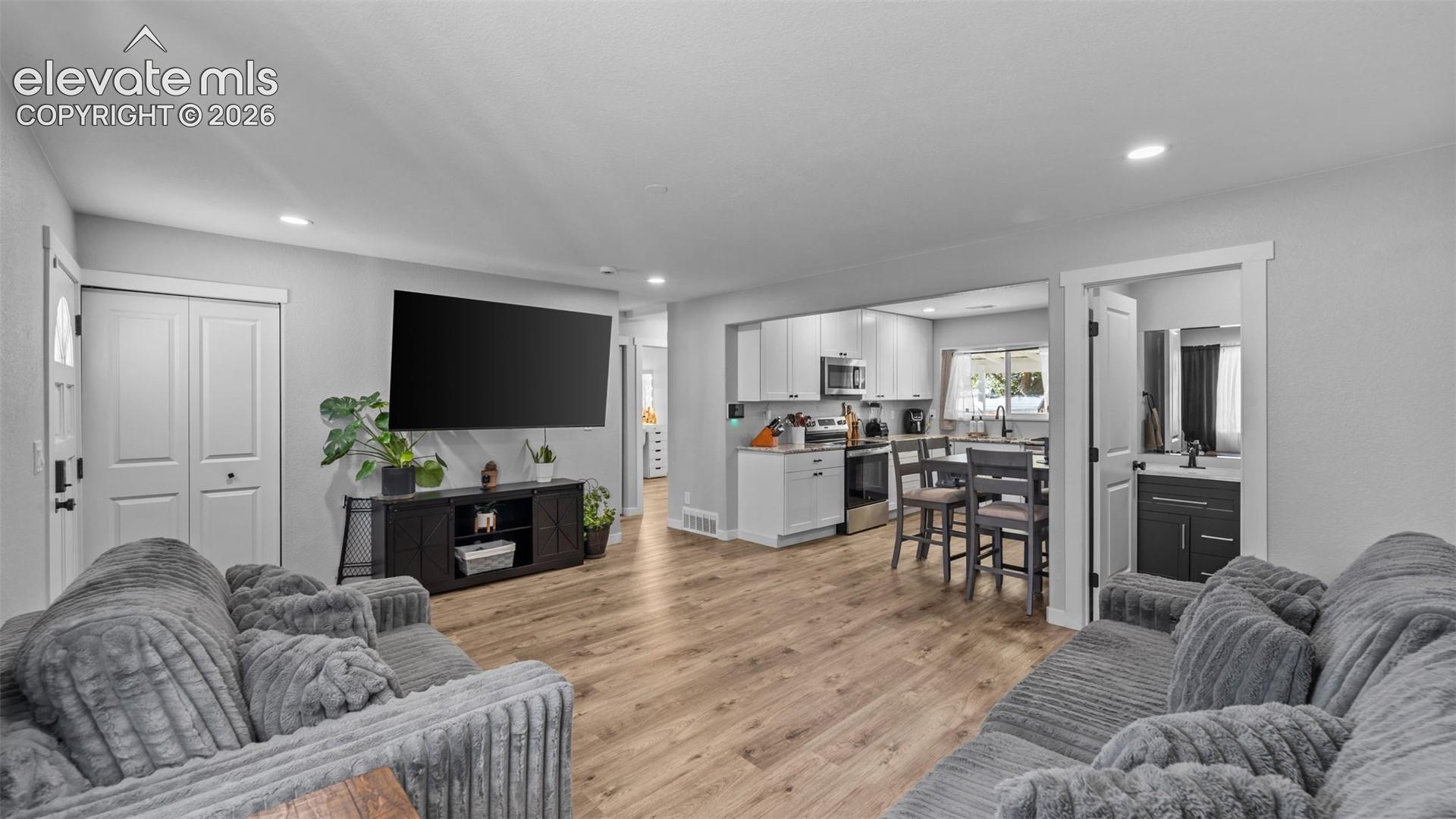 Open-concept interior featuring wood-finish flooring, recessed lighting, white shaker-style cabinetry, stainless steel appliances, and a dark-toned vanity with a rectangular sink