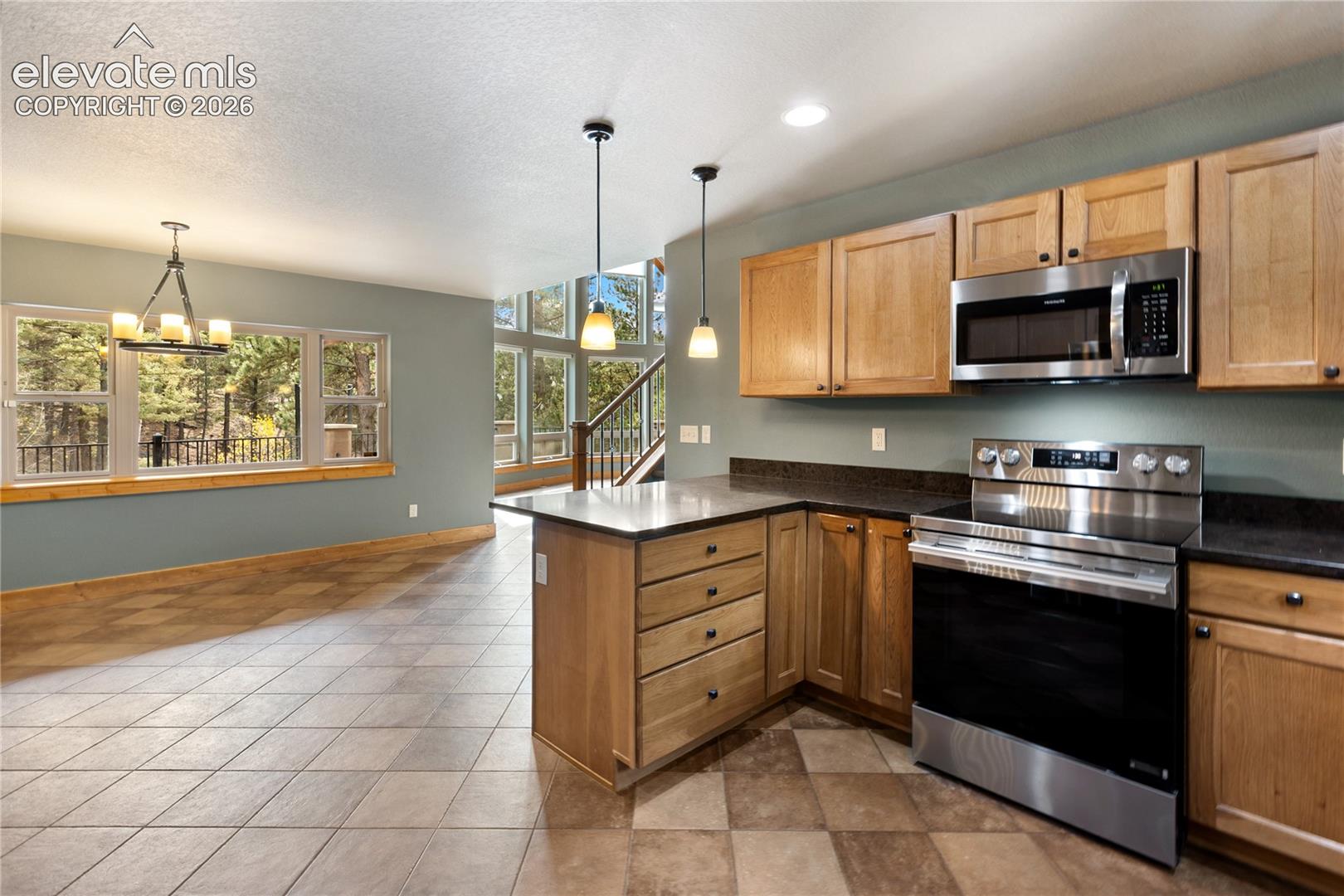 Kitchen featuring natural wood cabinetry, stone-finish countertops, stainless steel appliances, dual pendant lighting, and tile flooring