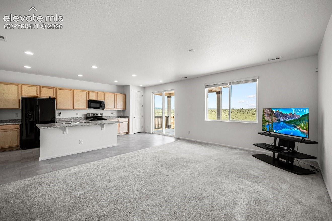 Open-concept living space with light wood cabinetry, a kitchen island, and recessed lighting