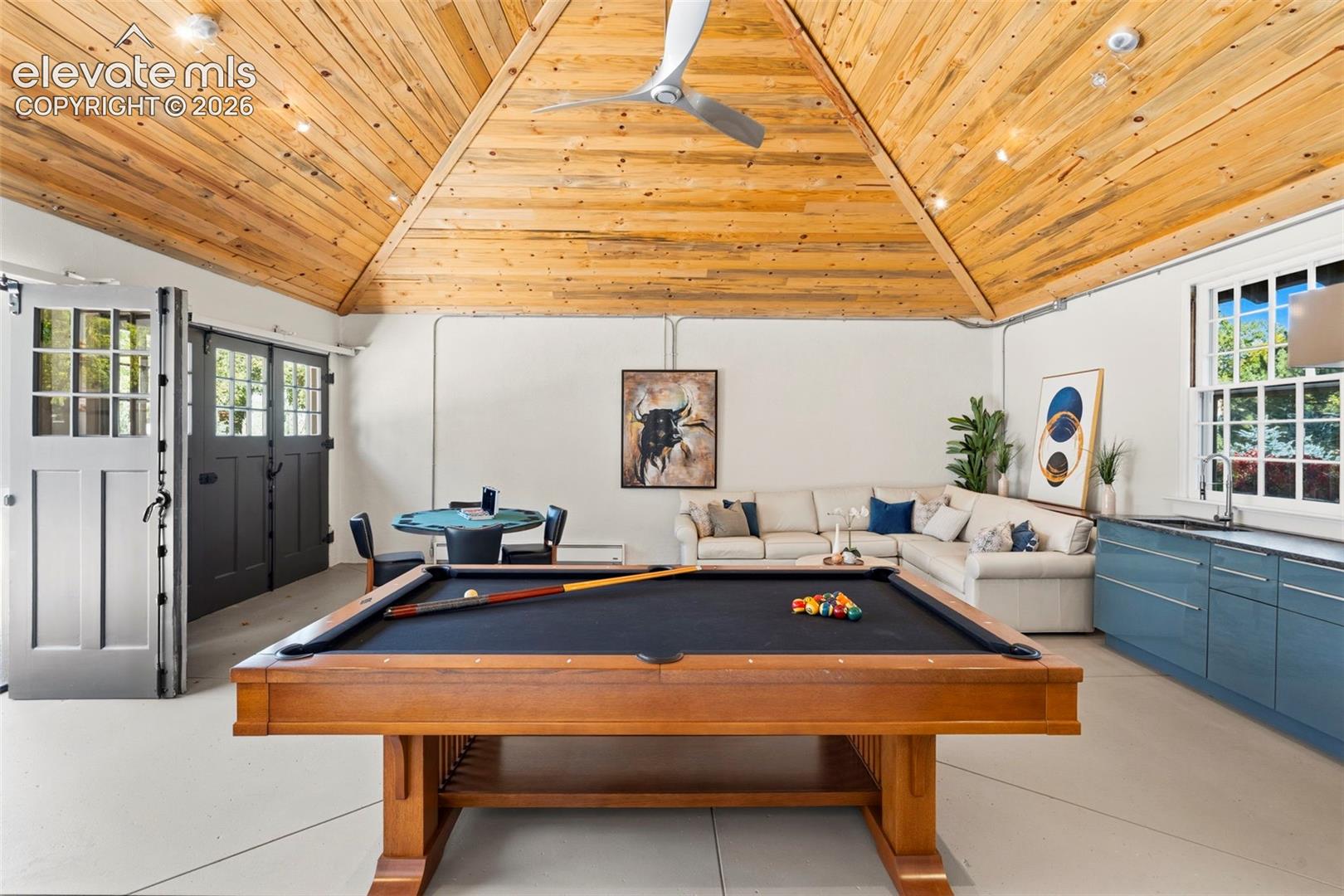 Vaulted wood-plank ceiling featuring a central ceiling fan, custom built-in blue cabinetry with a sink, double-door entry with glass panes, and recessed lighting