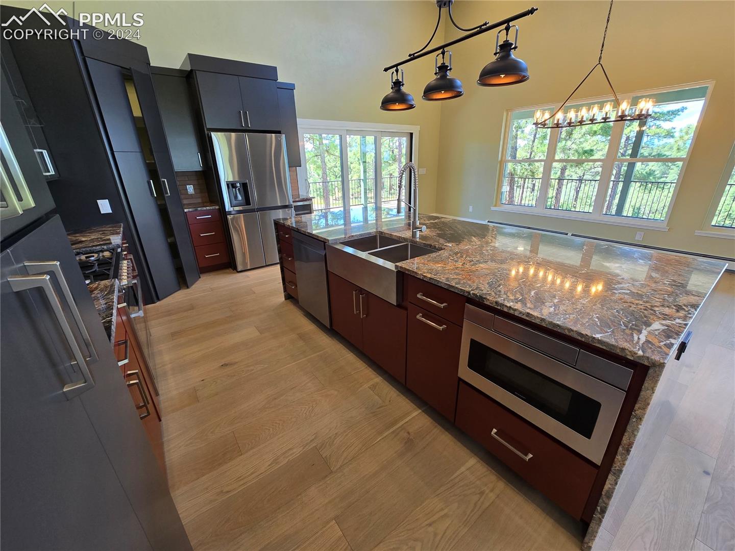 Kitchen featuring pendant lighting, light hardwood / wood-style flooring, stainless steel appliances, an island with sink, and sink