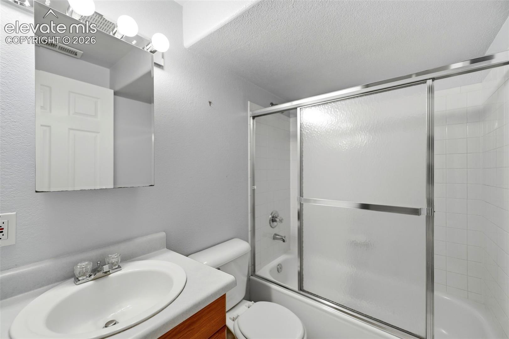 Bathroom featuring a wood-finish vanity with an integrated sink, a mirrored medicine cabinet, and a bathtub with a sliding glass enclosure