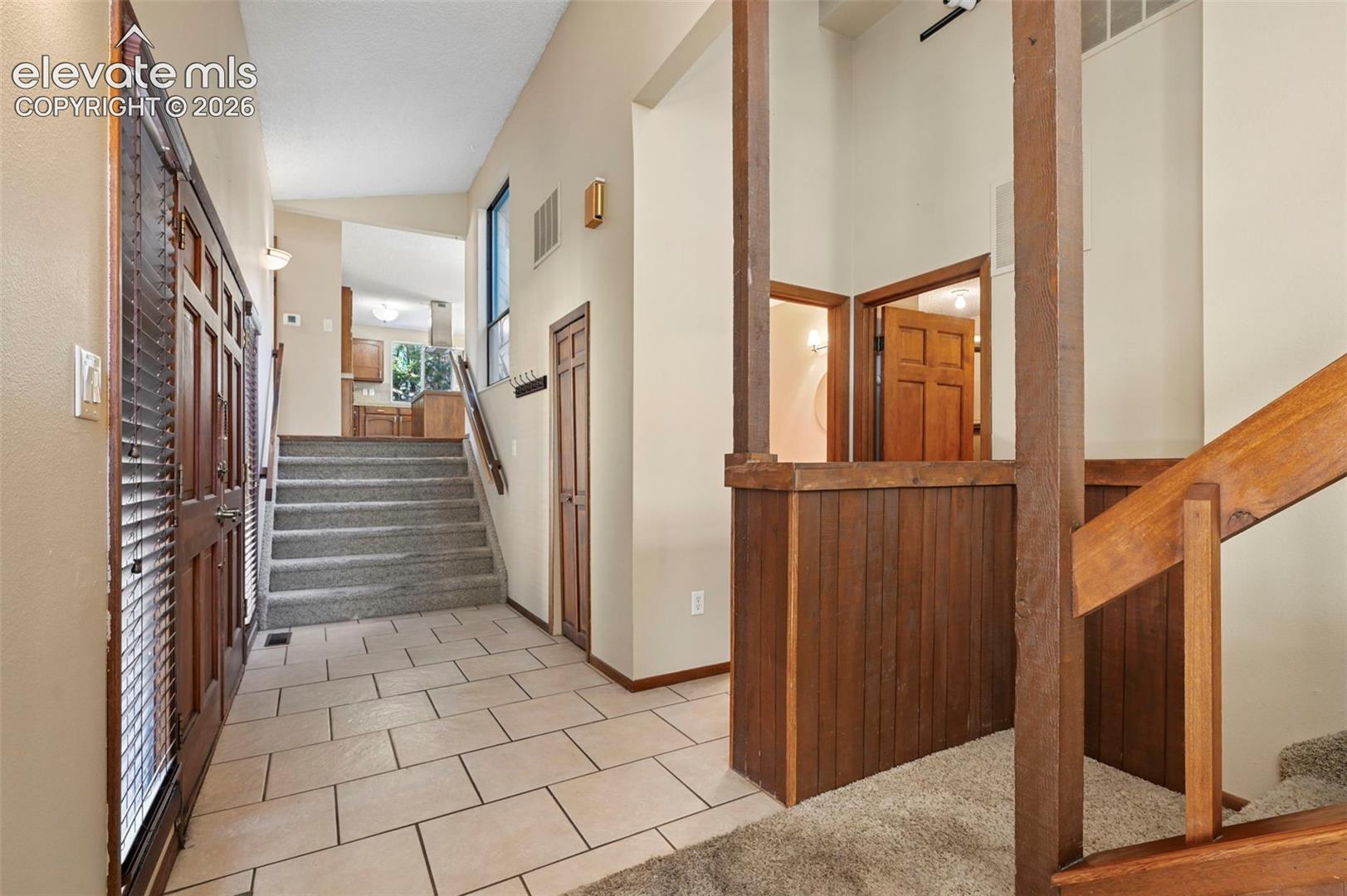 Entry featuring large-format tile flooring, vaulted ceilings, wood-paneled accents, and a dual-staircase configuration with wood railings