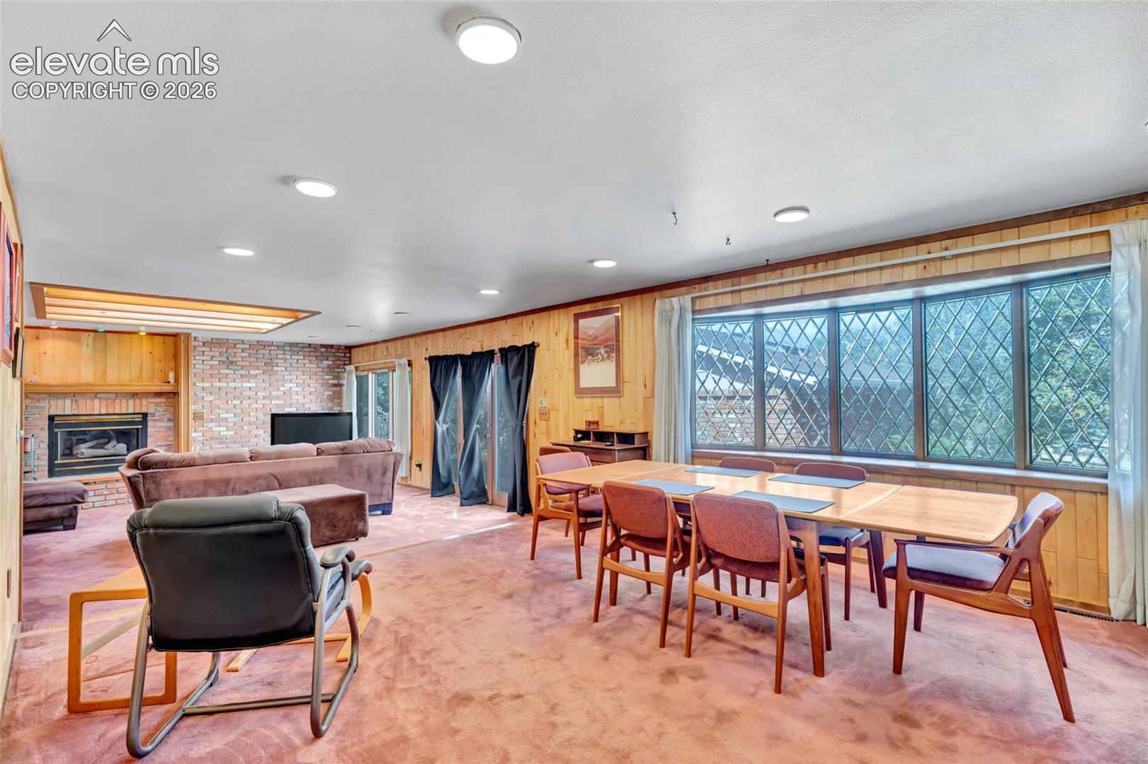 Open-concept living space featuring a brick fireplace surround, wood paneling, and recessed lighting