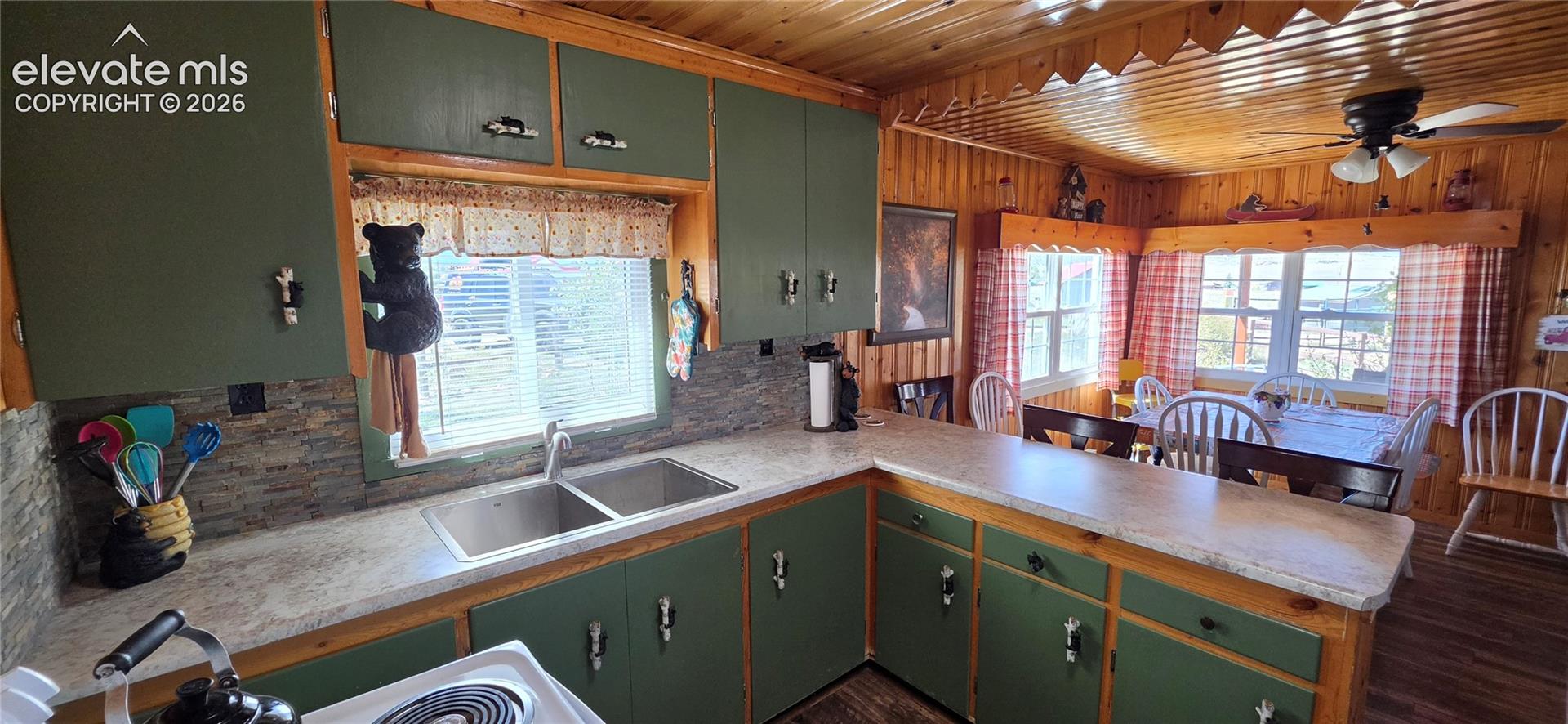 Kitchen featuring wood-paneled walls and ceiling, green cabinetry, and a dual basin stainless steel sink
