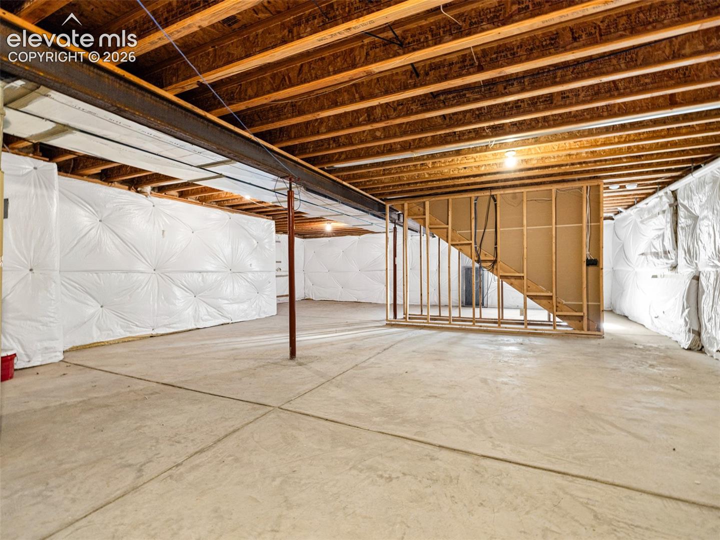 Unfinished basement with concrete flooring, visible wood ceiling joists, and a partial wood-framed wall
