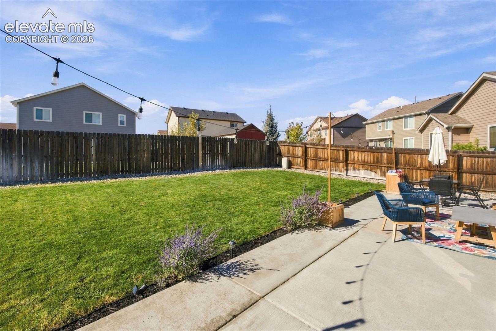 Fenced backyard featuring a concrete patio, grass lawn, and established perennial plantings