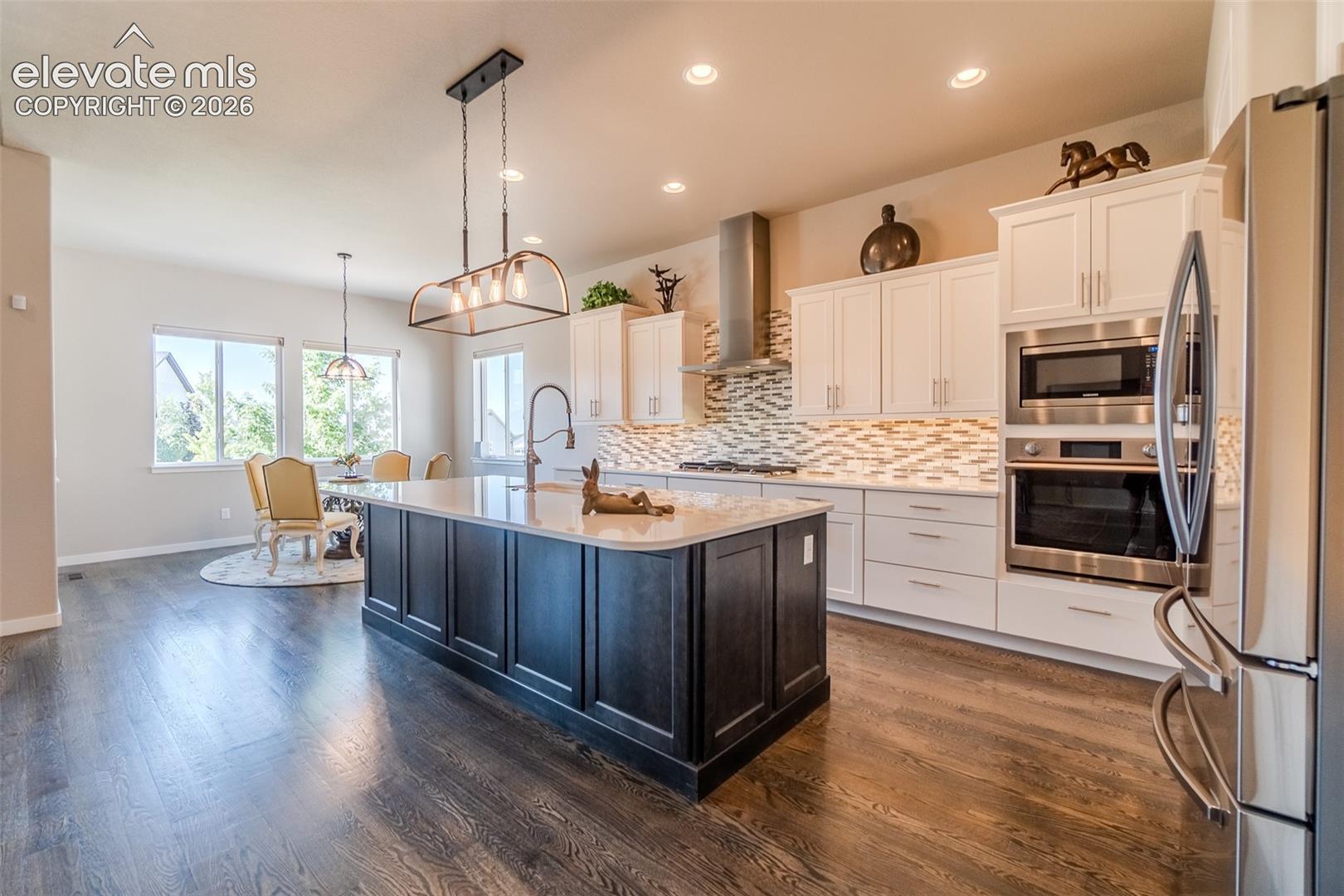 Gourmet kitchen featuring a large central island with light-toned countertop, white cabinetry with under-cabinet lighting, stainless steel appliances, and a unique tile backsplash