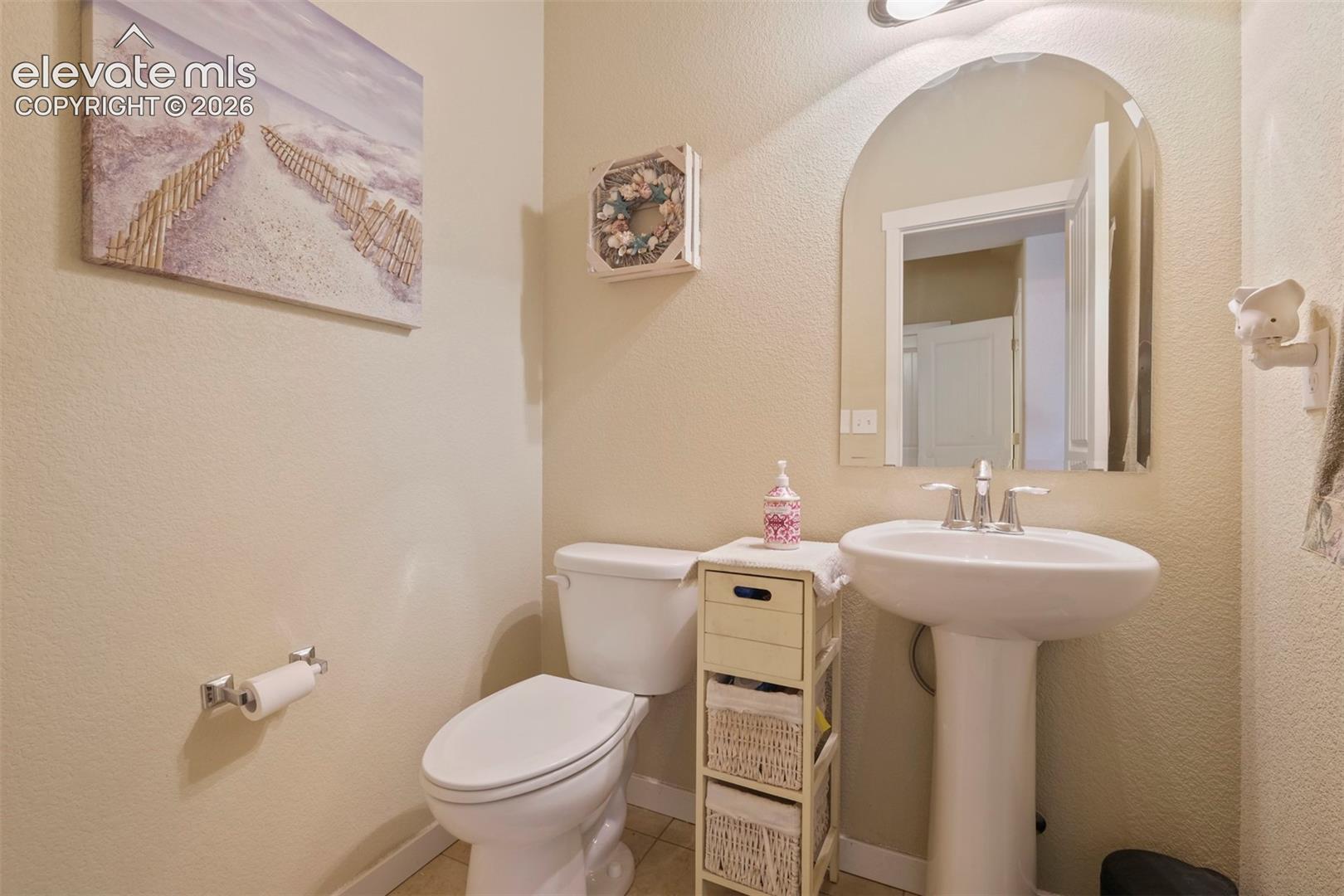 Main Level: Bathroom featuring a pedestal sink with chrome faucet, arched mirror, and commode