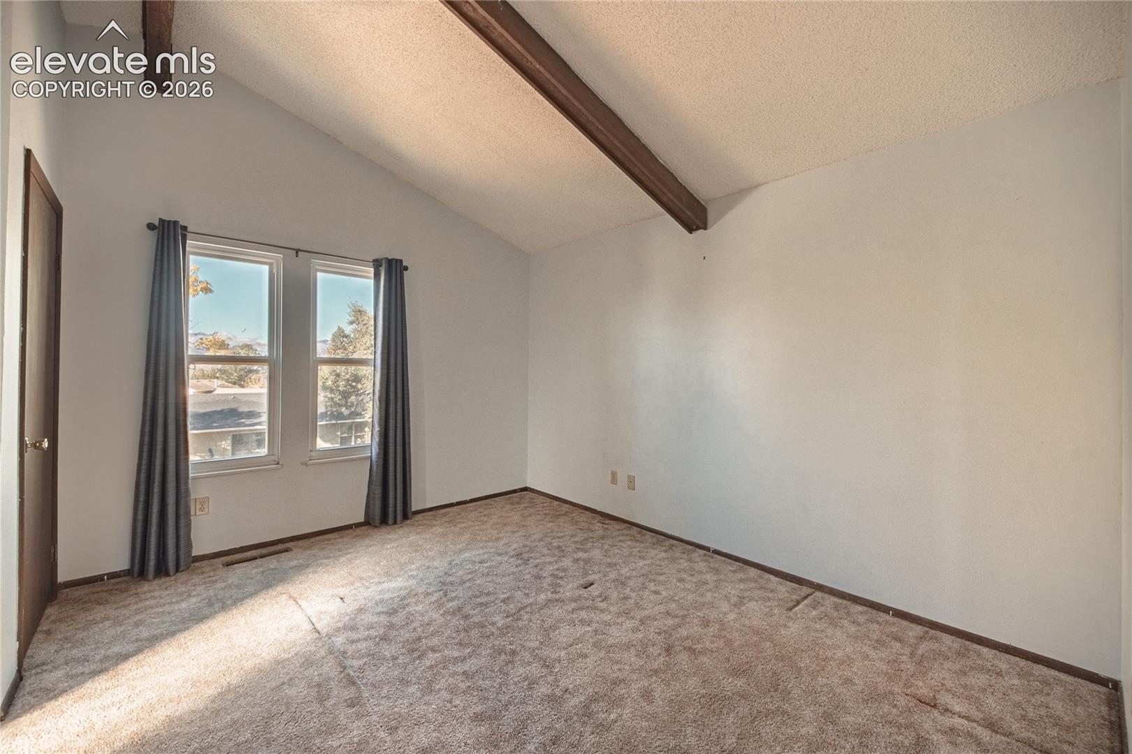 Vaulted ceiling featuring exposed structural beams, dual windows, and wall-to-wall carpeting