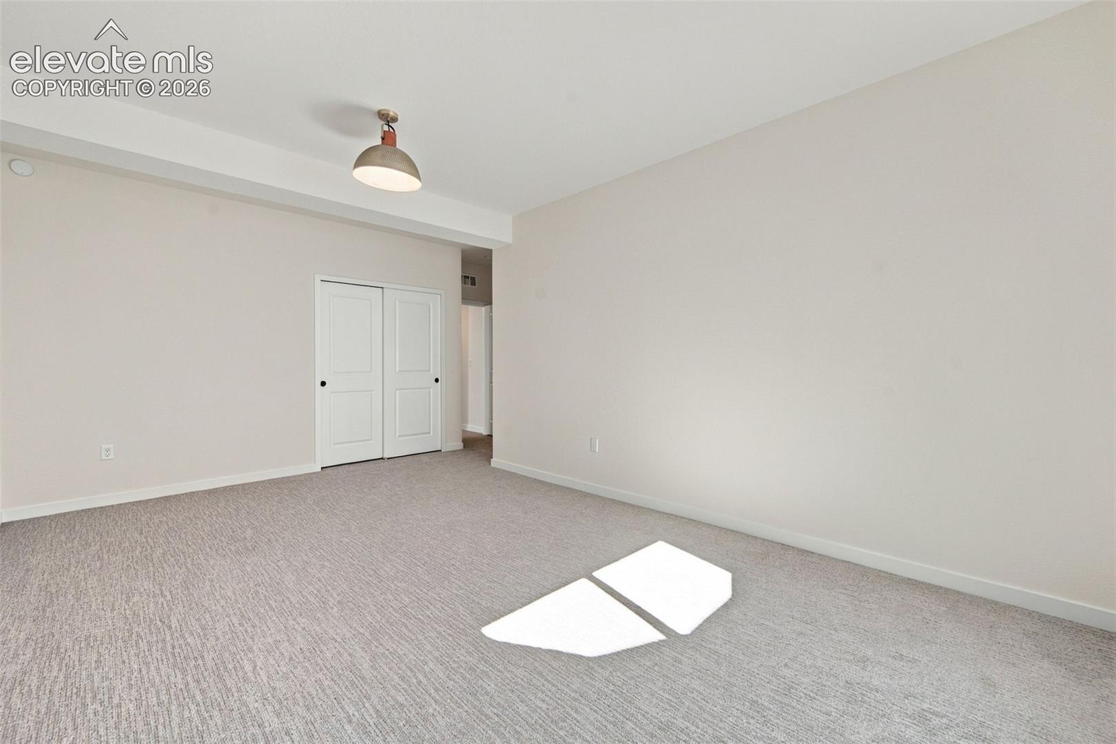 Neutral-toned interior space featuring wall-to-wall carpeting, a semi-flush mount ceiling fixture, and two-panel closet doors