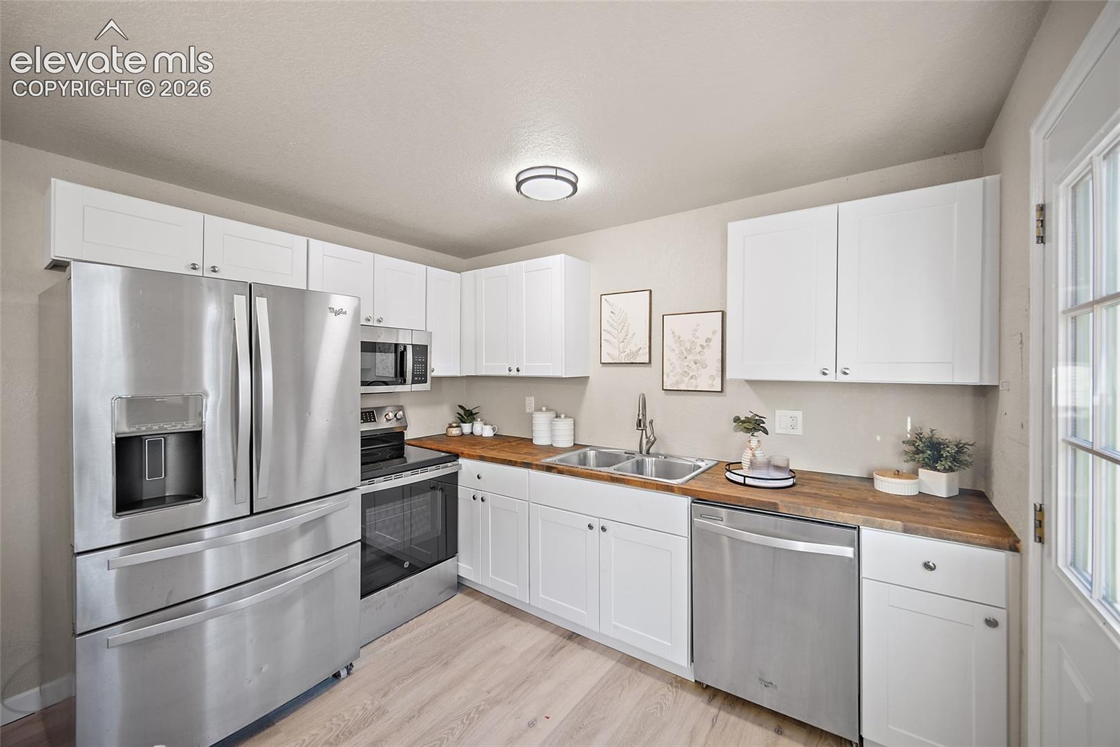 Modern kitchen featuring white cabinetry, stainless steel appliances, butcher block countertops, a double basin sink, and wood-finish flooring
