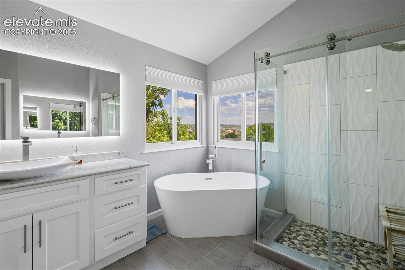 Modern bathroom featuring a freestanding soaking tub, a frameless glass-enclosed shower with pebble flooring, and  dual vanities with vessel sinks. 
