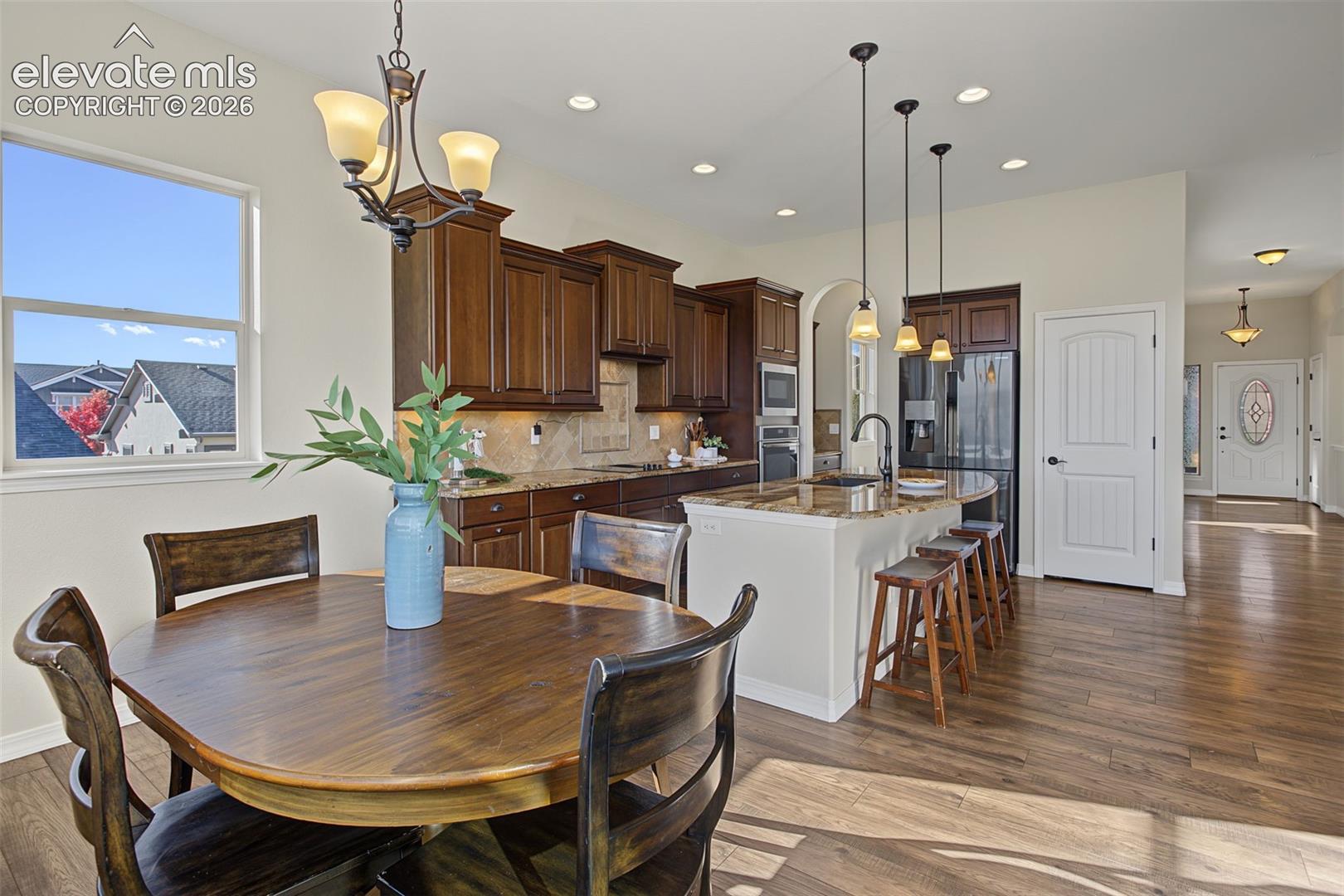 Kitchen featuring wood-finish cabinetry, stone countertops, a center island with pendant lighting, a tile backsplash, and wood-finish flooring