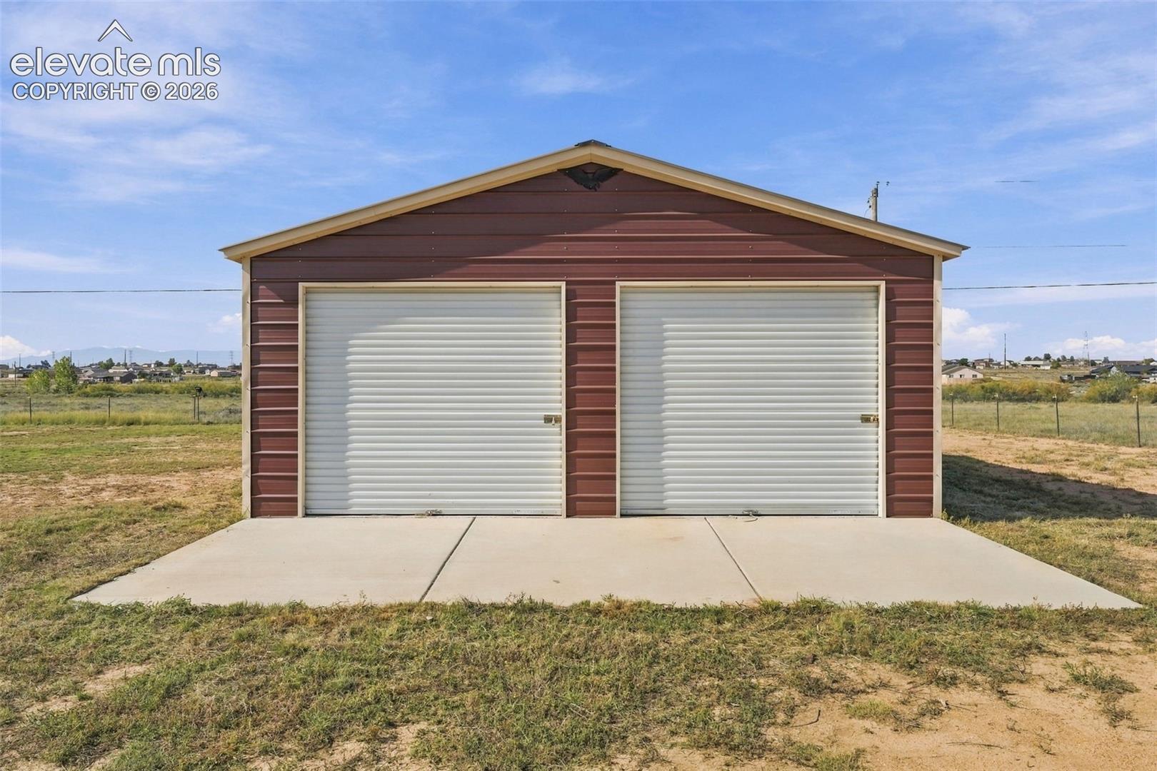 Detached structure featuring metal siding, a gabled roof, two roll-up doors, and a concrete apron