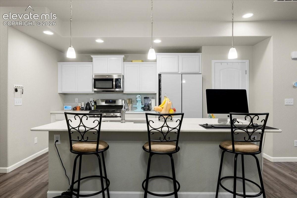 Kitchen featuring an island with countertop, white cabinetry, stainless steel microwave, and wood-finish flooring
