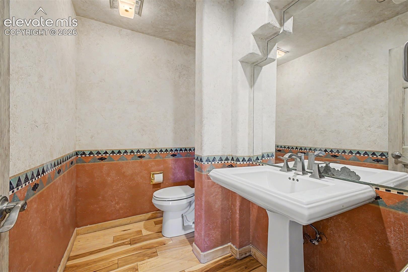 Pedestal sink with brushed nickel fixtures, wood-finish flooring, and decorative wall tiling