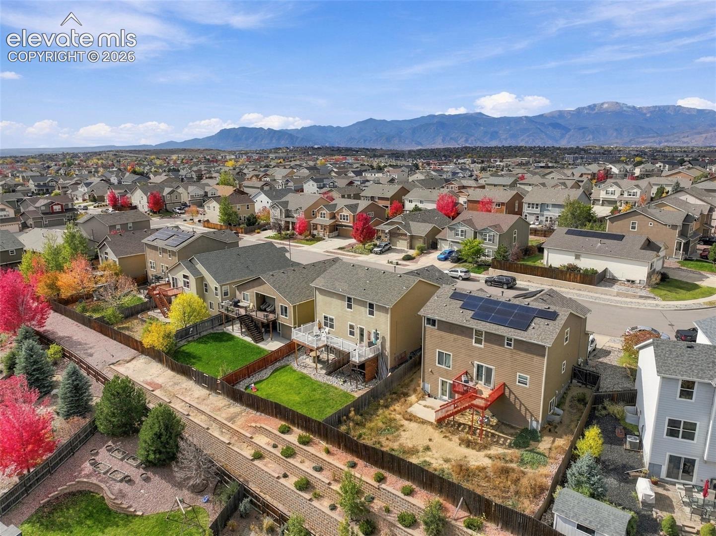 Aerial perspective showcasing multi-level residential properties featuring roof-mounted solar panels, wood-slat fencing, elevated rear decks, and expansive mountain range backdrop