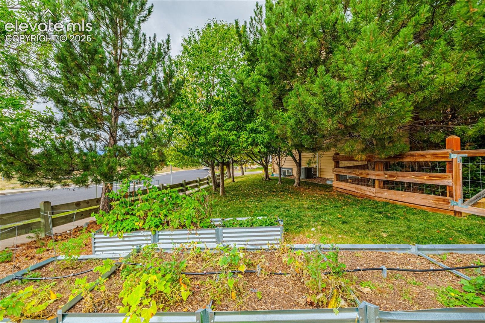Landscaped yard featuring raised garden beds, mature trees, and a wooden perimeter fence