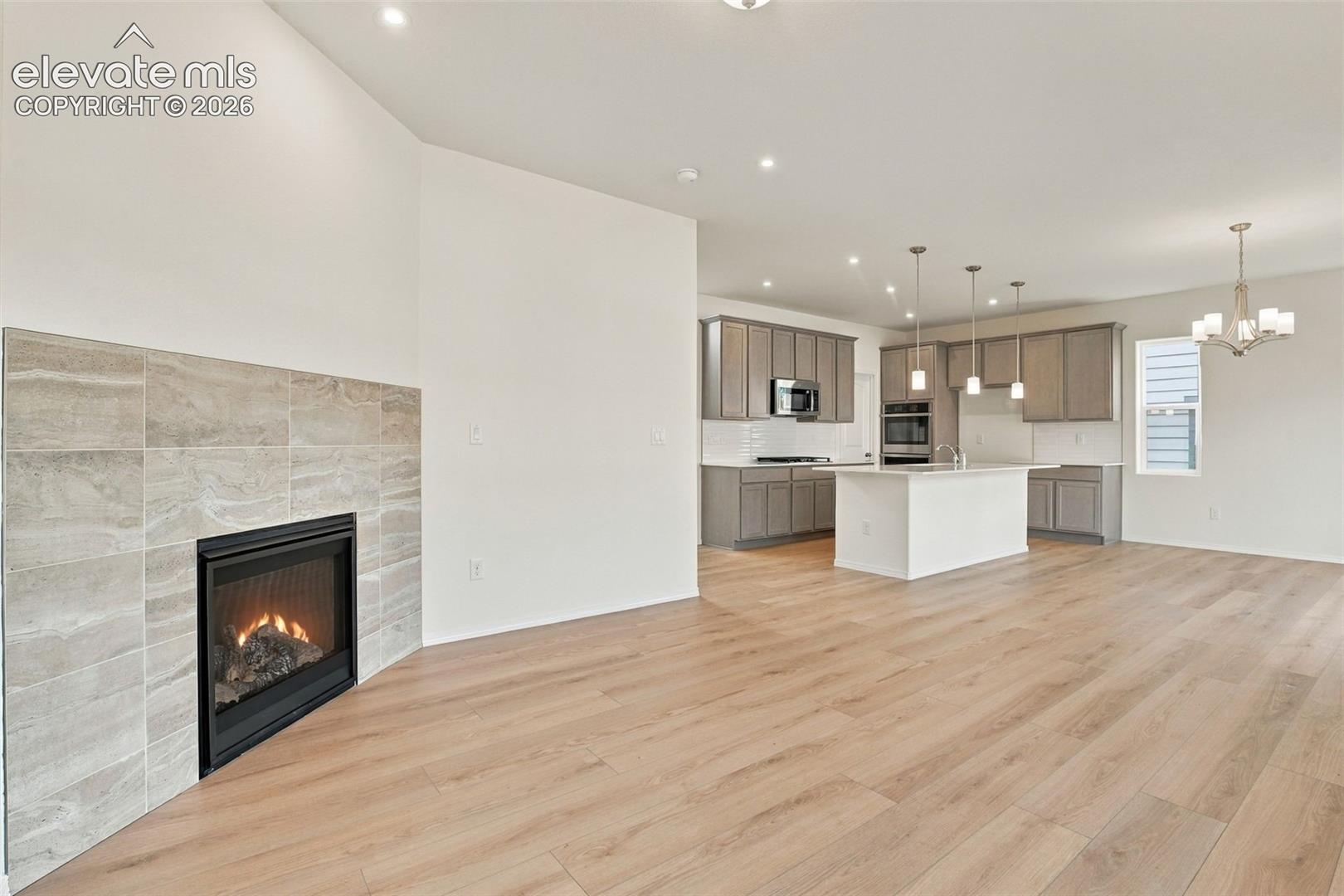 Gas fireplace with tile surround, wood-finish flooring, central kitchen island, built-in cabinetry, and recessed lighting