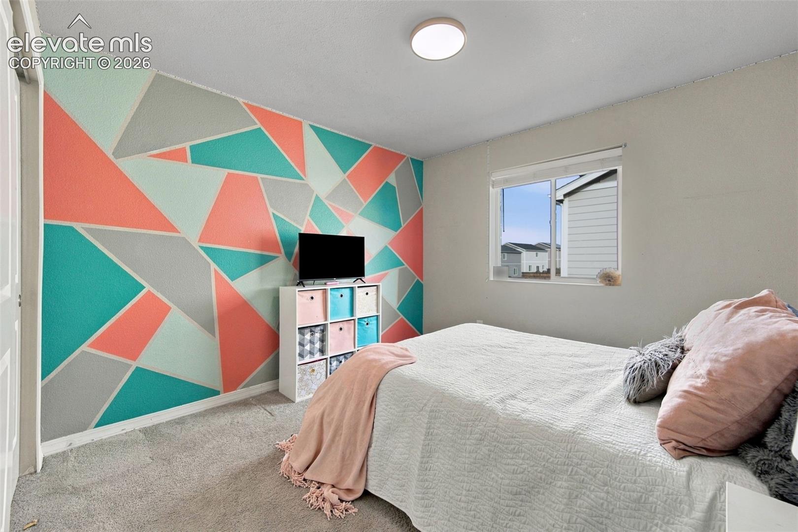 Room featuring a geometric accent wall, wall-to-wall carpeting, flush-mount ceiling lighting, and a window with a horizontal slider