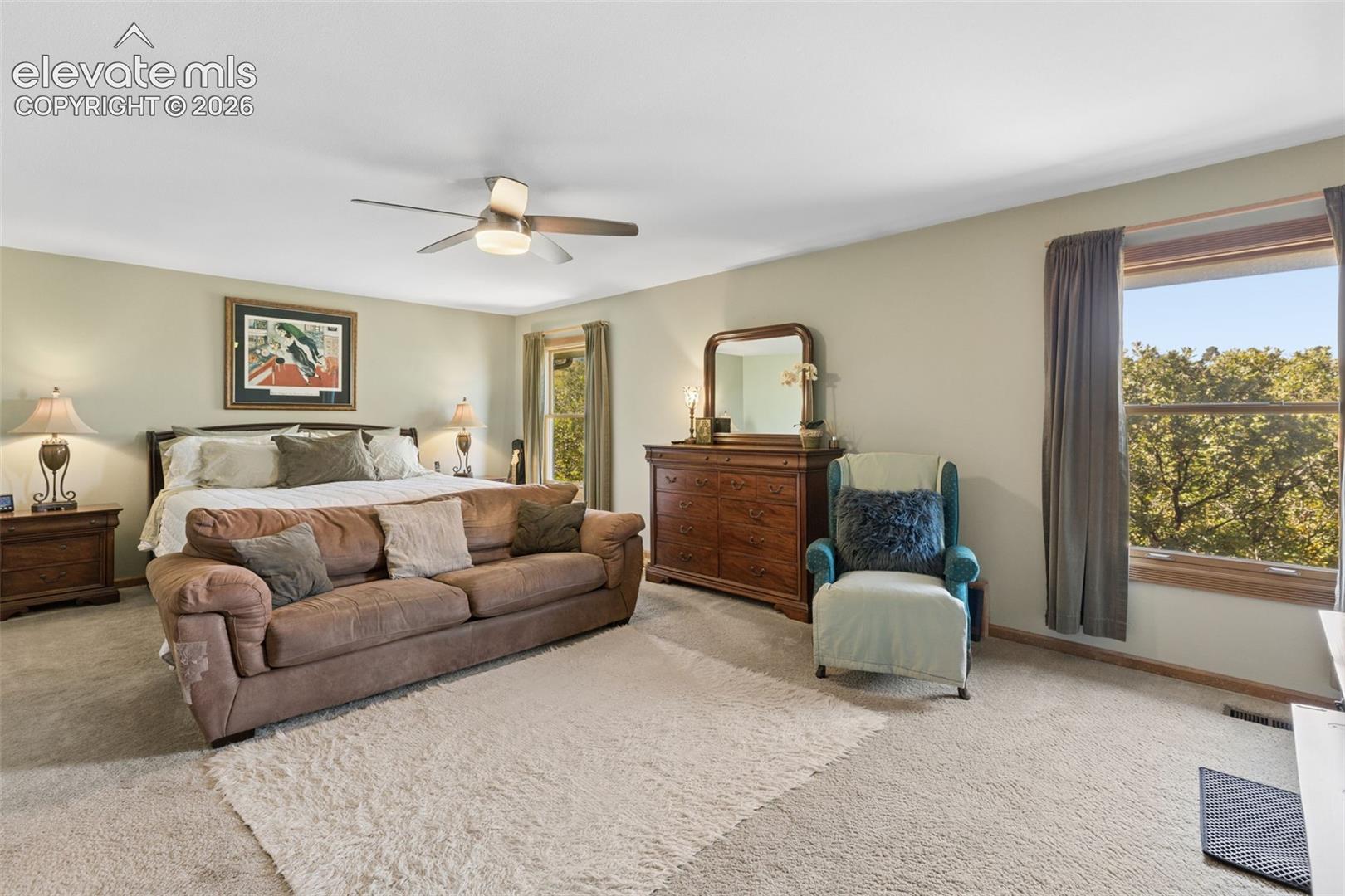 Spacious interior featuring neutral carpeting, a dual-blade ceiling fan with integrated lighting, and large windows with wooden trim