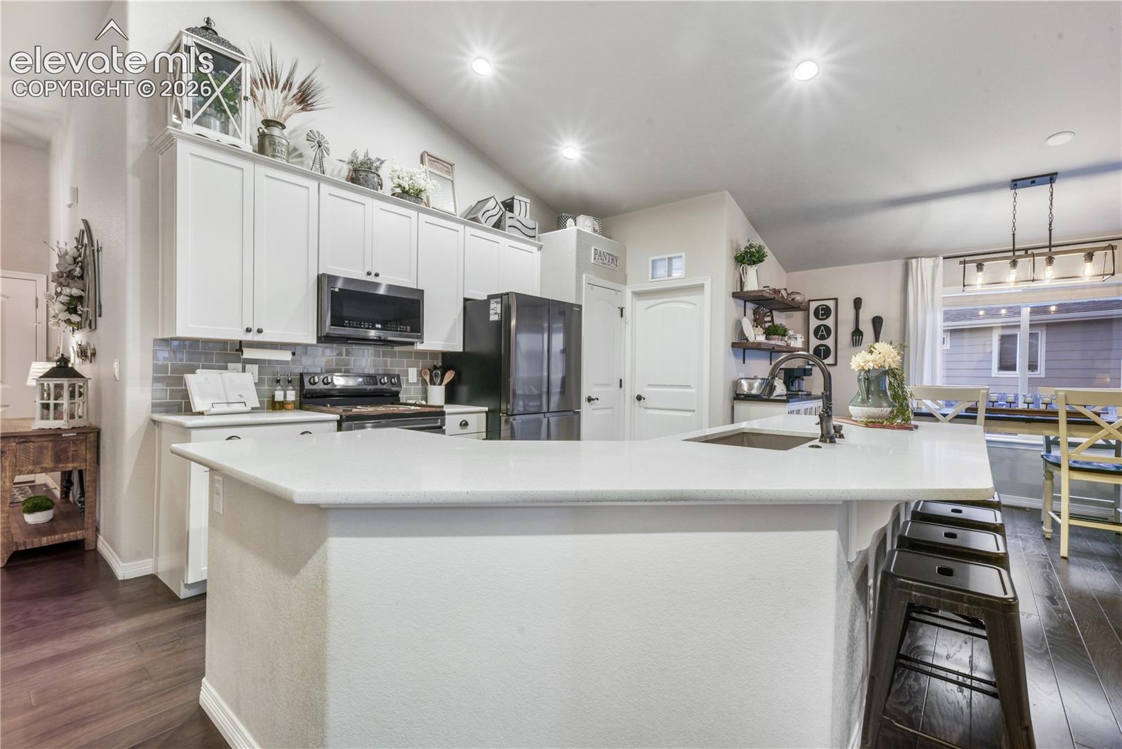 Kitchen featuring white cabinetry, a large kitchen island with a built-in sink, dark wood-finish flooring, recessed lighting, and a subway tile backsplash