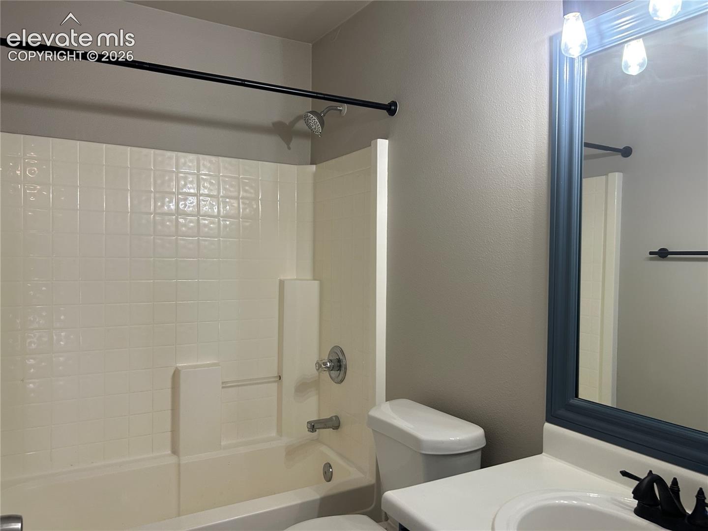 Bathroom featuring a tub and shower combination with tiled surround, a vanity with a white countertop, a framed wall-mounted mirror, and matte black fixtures