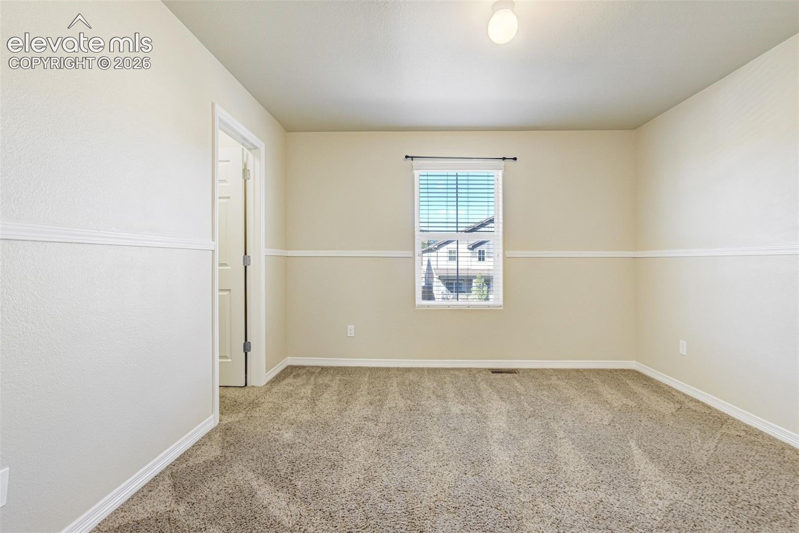 Neutral-toned wall paint, textured carpeting, window with blinds, overhead flush mount light fixture, and white trim molding