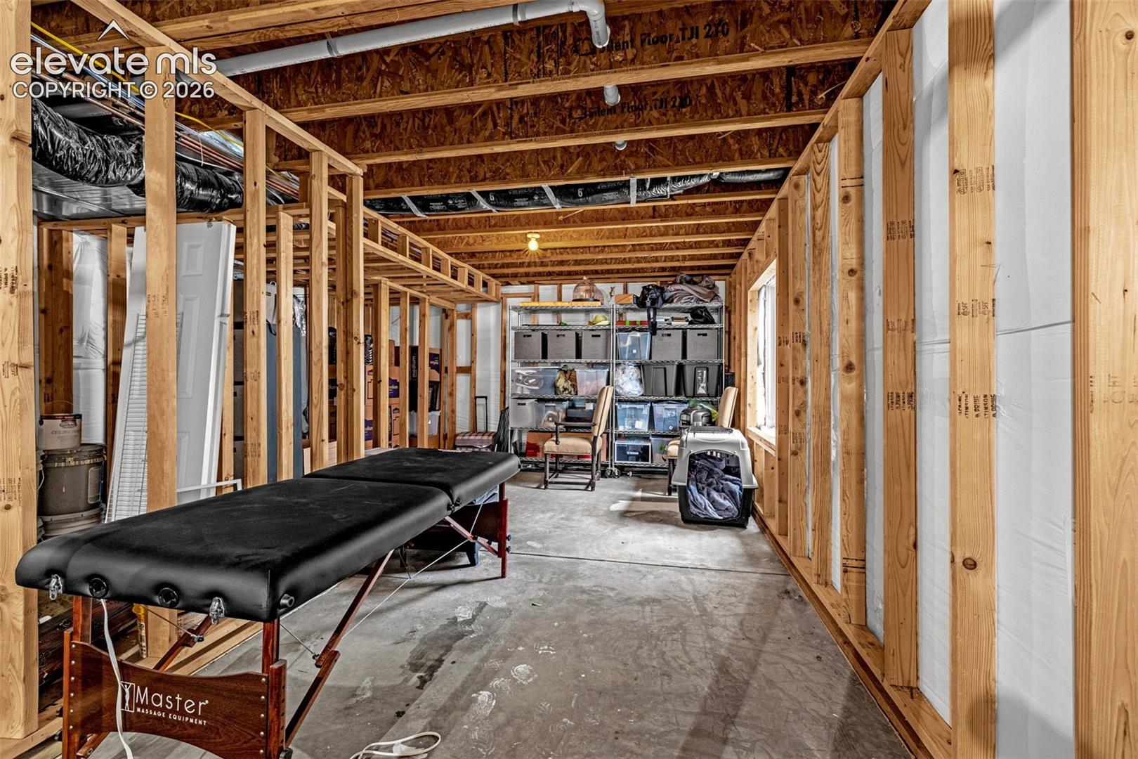 Unfinished interior space featuring exposed wood-stud framing, exposed floor joists, and concrete flooring