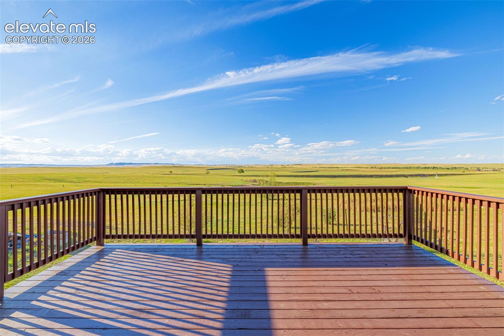 Expansive outdoor deck with wood-finish flooring and full railing system, overlooking open green terrain