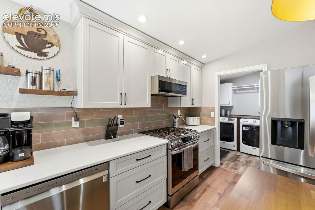 White shaker cabinetry, stainless steel appliances, white countertops, subway tile backsplash, and wood-finish flooring
