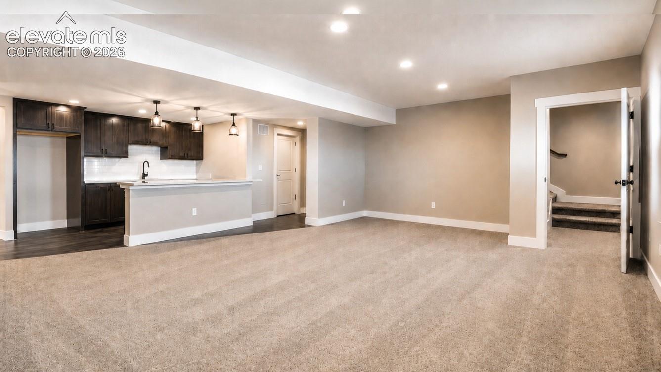 Expansive open-concept room featuring plush carpeting, recessed lighting, a built-in wet bar with dark wood cabinetry, a subway tile backsplash, and pendant lighting