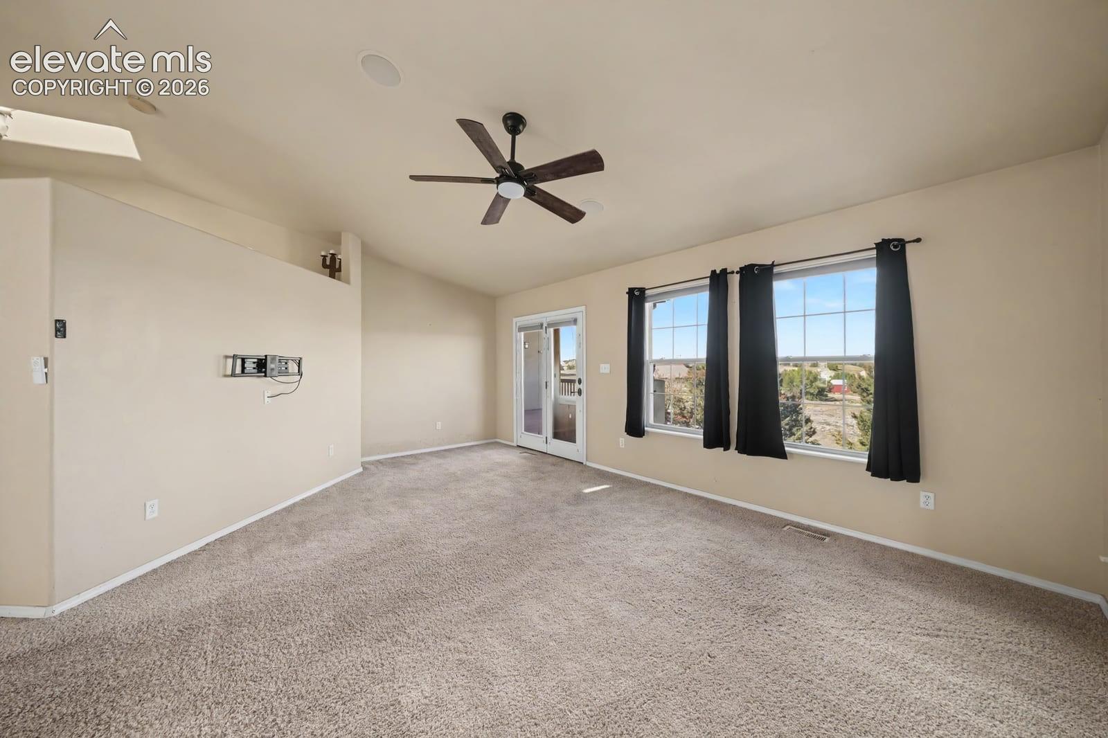 Spacious interior featuring high ceilings, neutral wall-to-wall carpeting, a ceiling fan, and large windows providing natural light