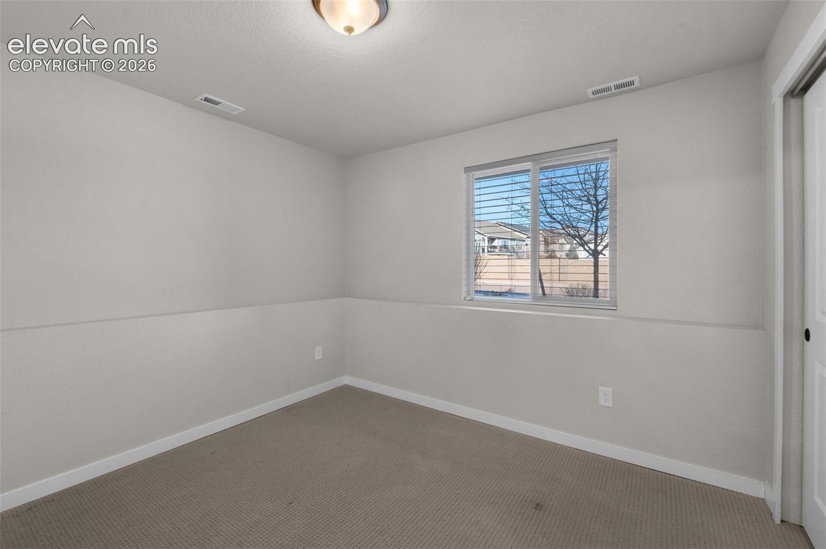 Neutral-toned carpeting, white walls, and a window with horizontal blinds