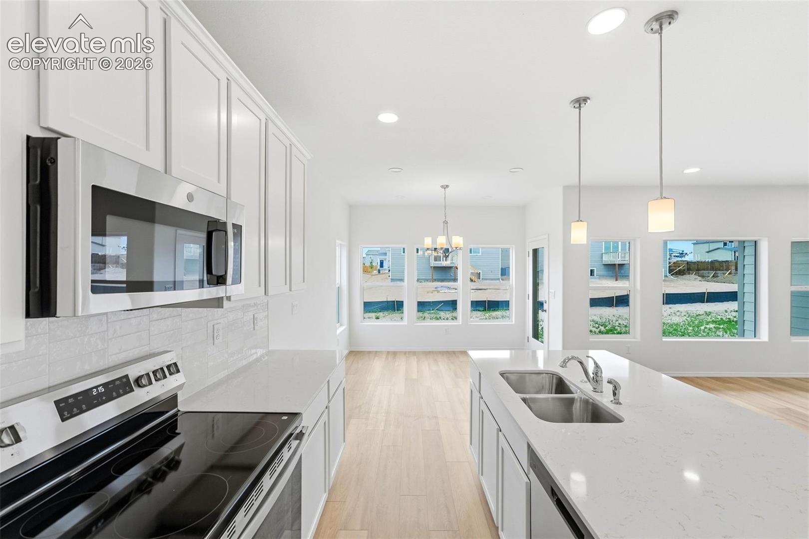 Kitchen featuring white shaker-style cabinetry, quartz countertops, stainless steel appliances, a central island with an undermount double-basin sink, and wood-finish flooring