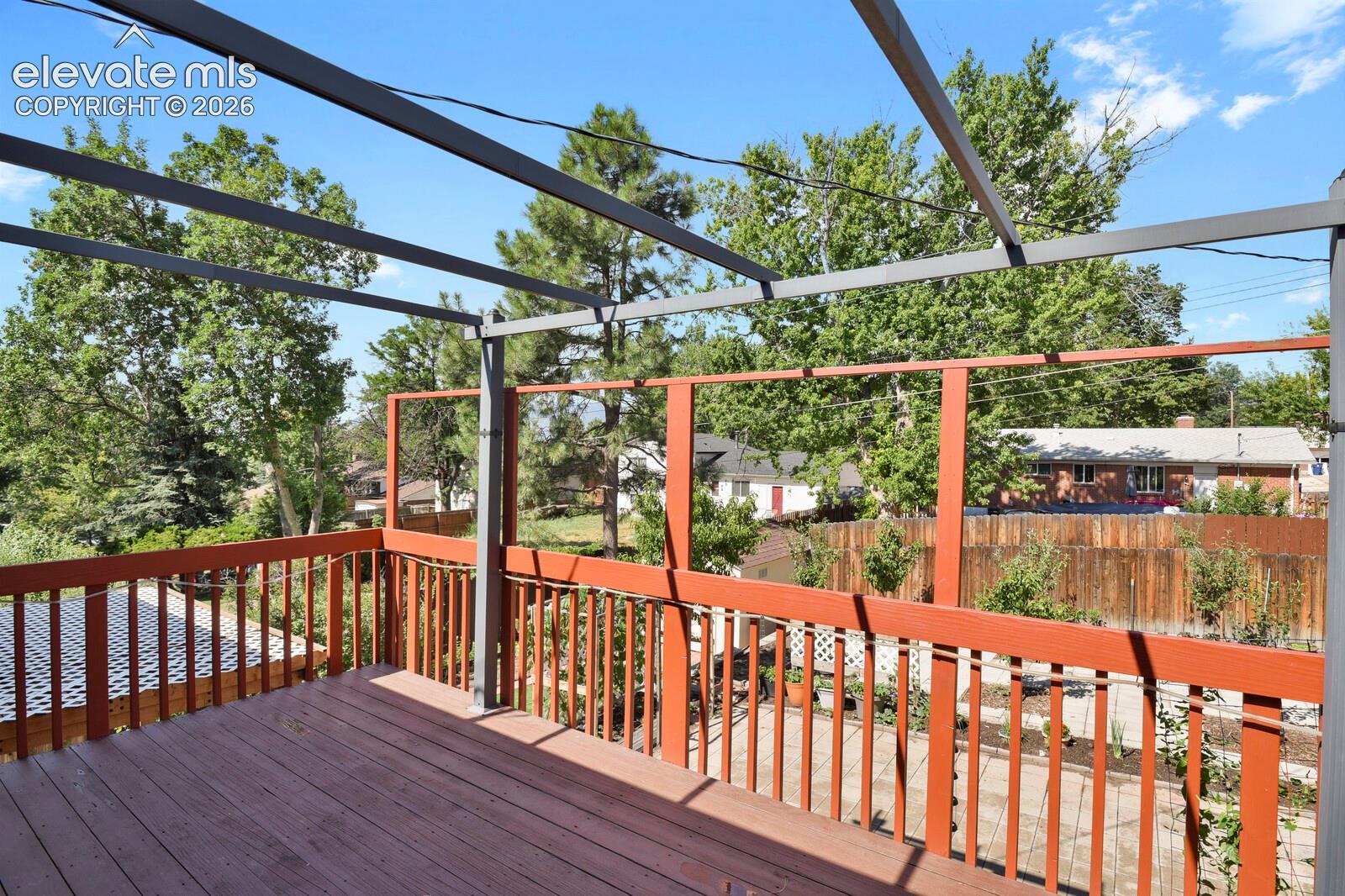 Expansive composite deck featuring rich wood-finish flooring, horizontal metal railings, and integrated pergola structure with overhead beams providing shade