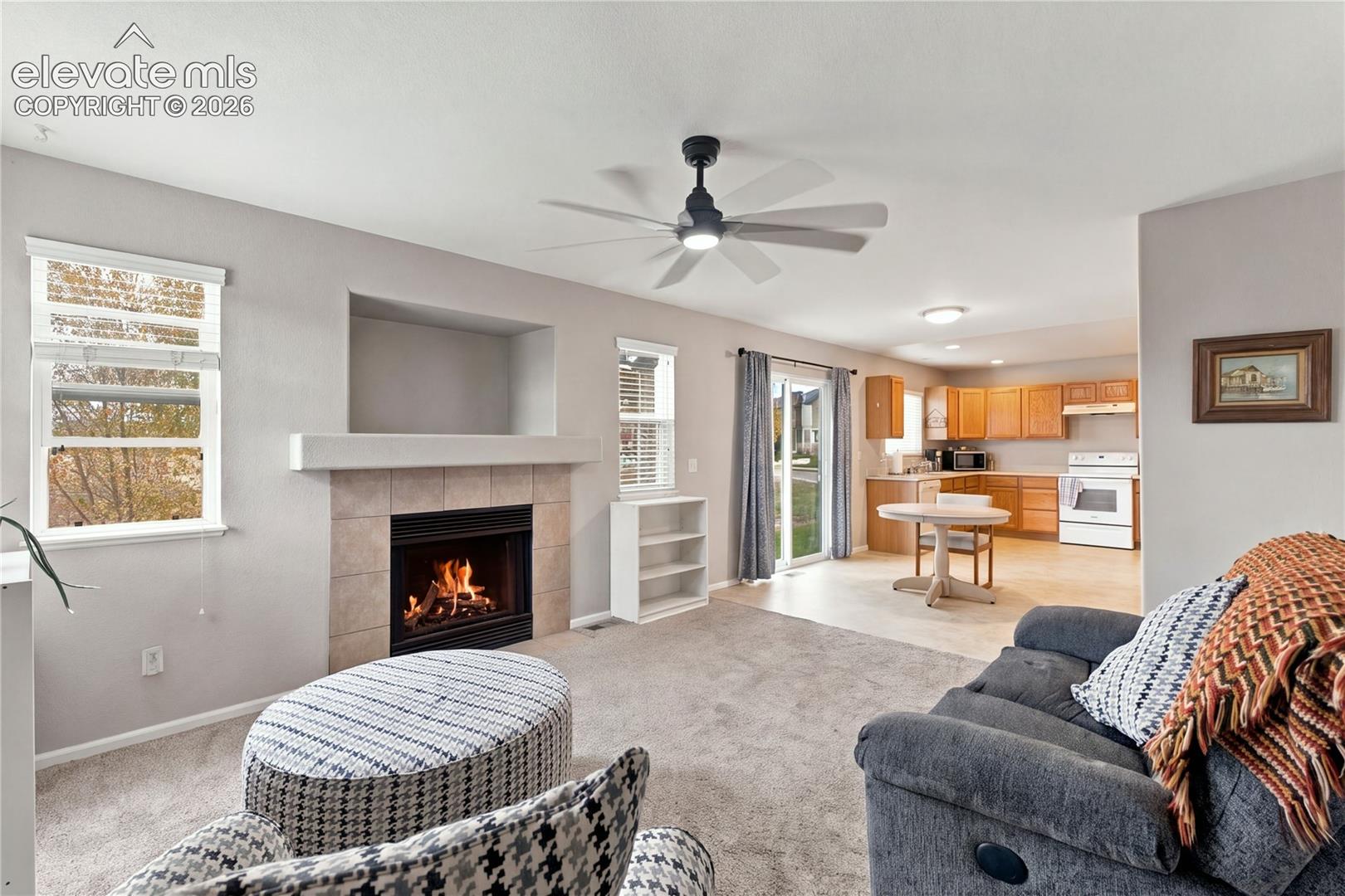 Living area featuring a tile-surround fireplace with built-in media niche, neutral wall-to-wall carpeting, ceiling fan, and sliding glass door