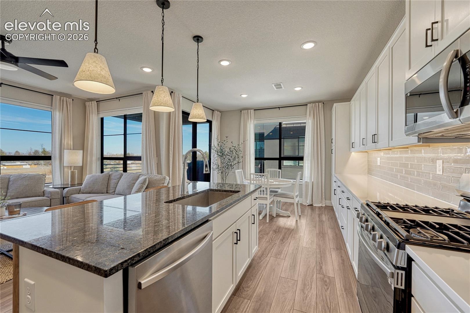Kitchen featuring a large central island with a stone countertop and undermount sink, white cabinetry, a subway tile backsplash, stainless steel appliances, and wood-finish flooring
