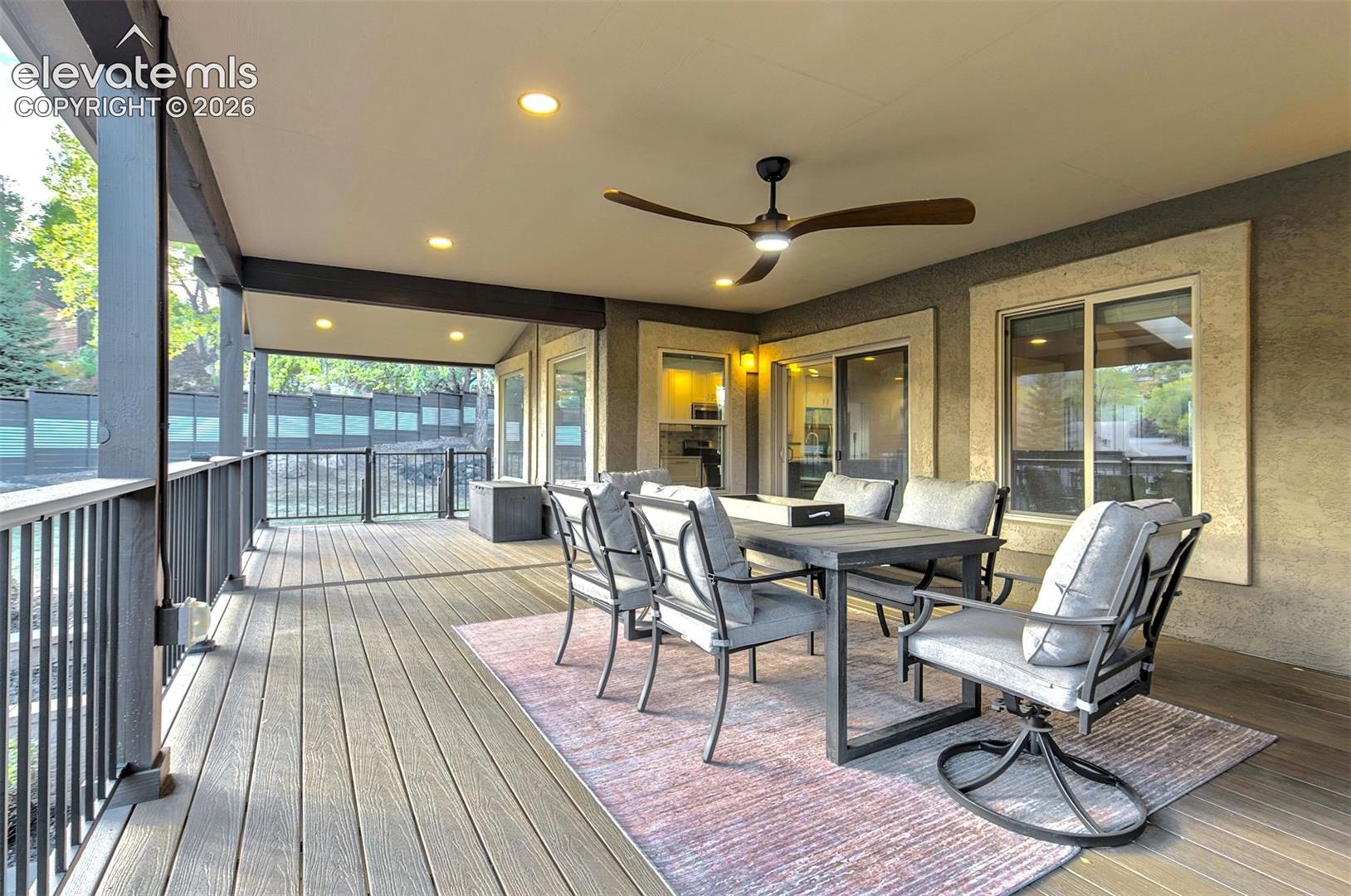 Covered outdoor deck featuring wood-finish decking, integrated recessed lighting, a modern ceiling fan, and black metal railings
