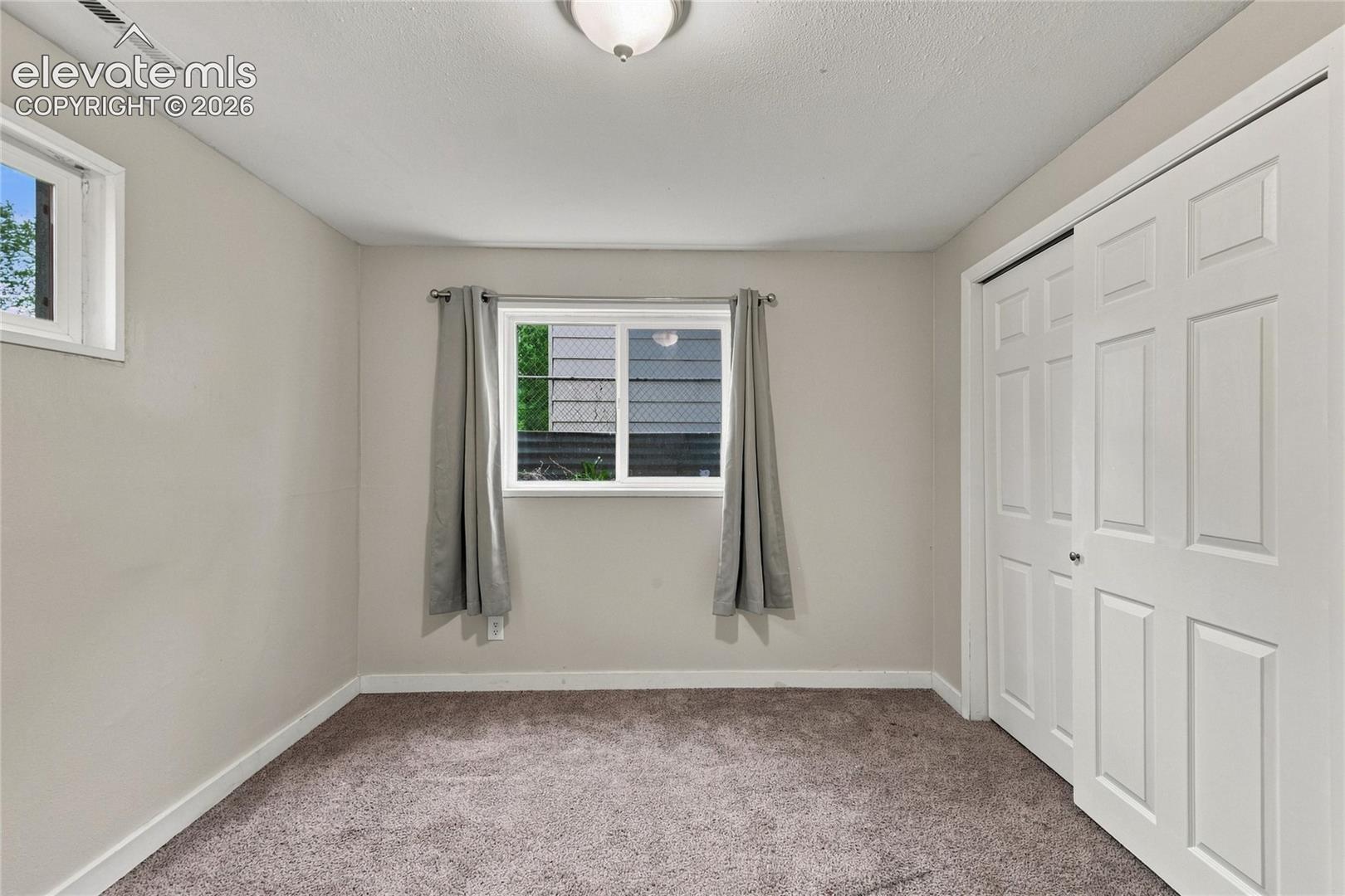 Basement bedroom with carpet flooring, white trim, and two windows provide natural light