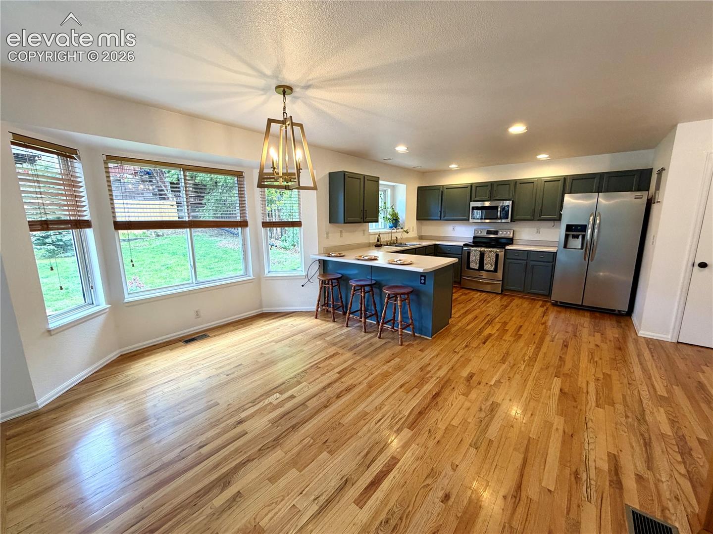 Open-concept kitchen and dining area featuring wood-finish flooring, a bay window, and a contemporary chandelier