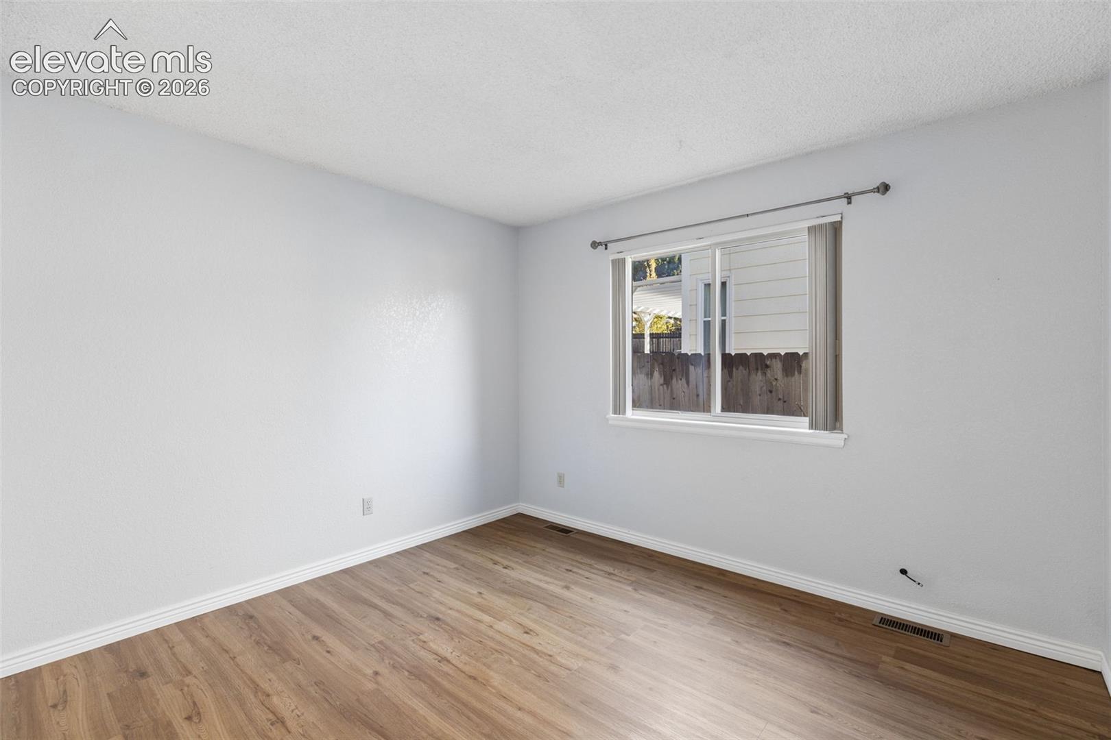 Interior room featuring wood-finish flooring, neutral walls, a sliding window with horizontal blinds, and a metal curtain rod
