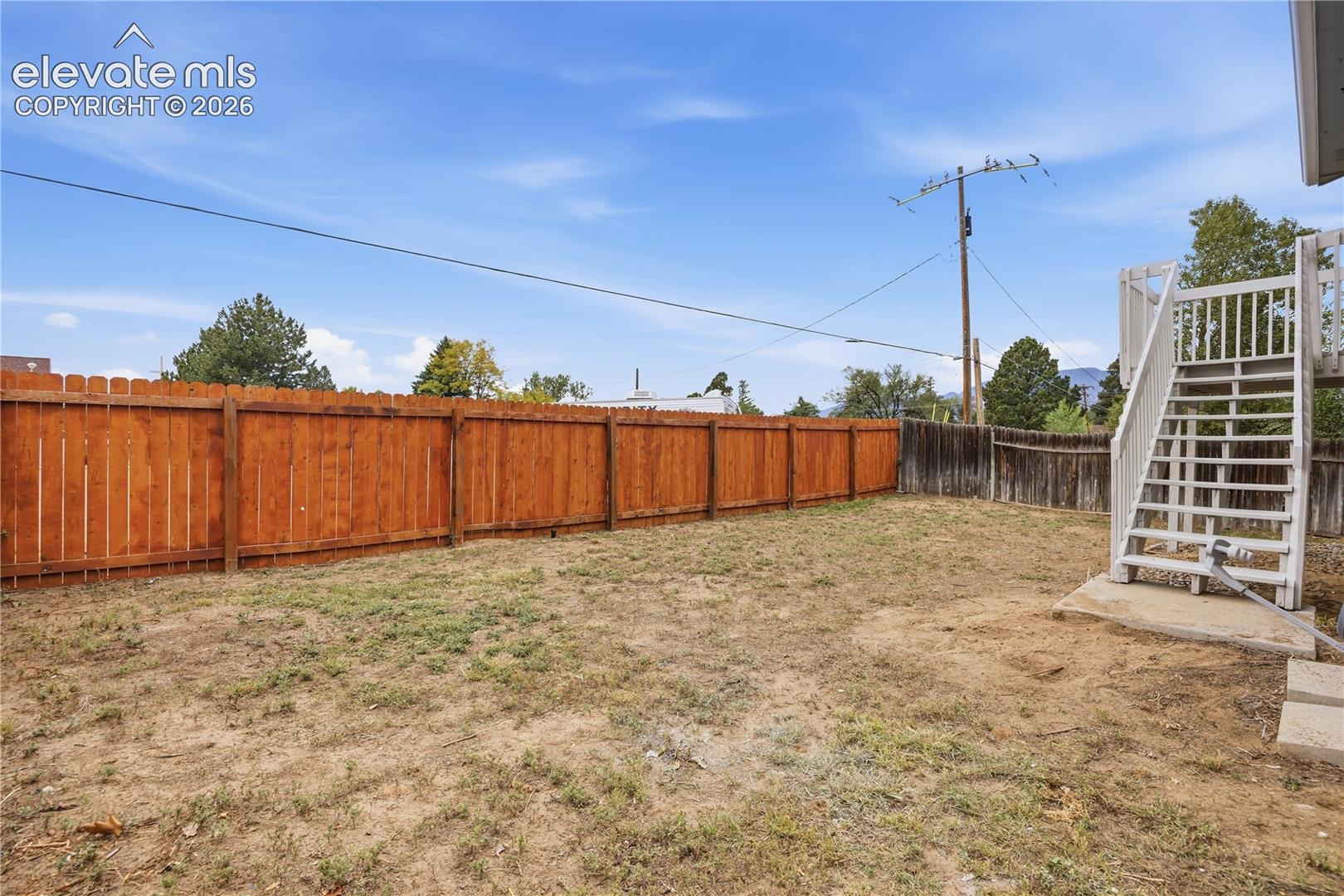 Backyard area featuring a wood privacy fence, exterior wooden staircase, and concrete landing