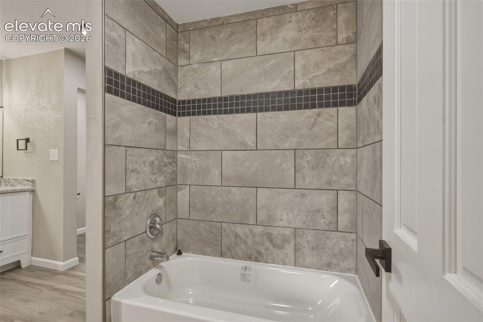 Bathtub with integrated shower, gray large-format tile surround, mosaic accent band, and chrome fixtures
